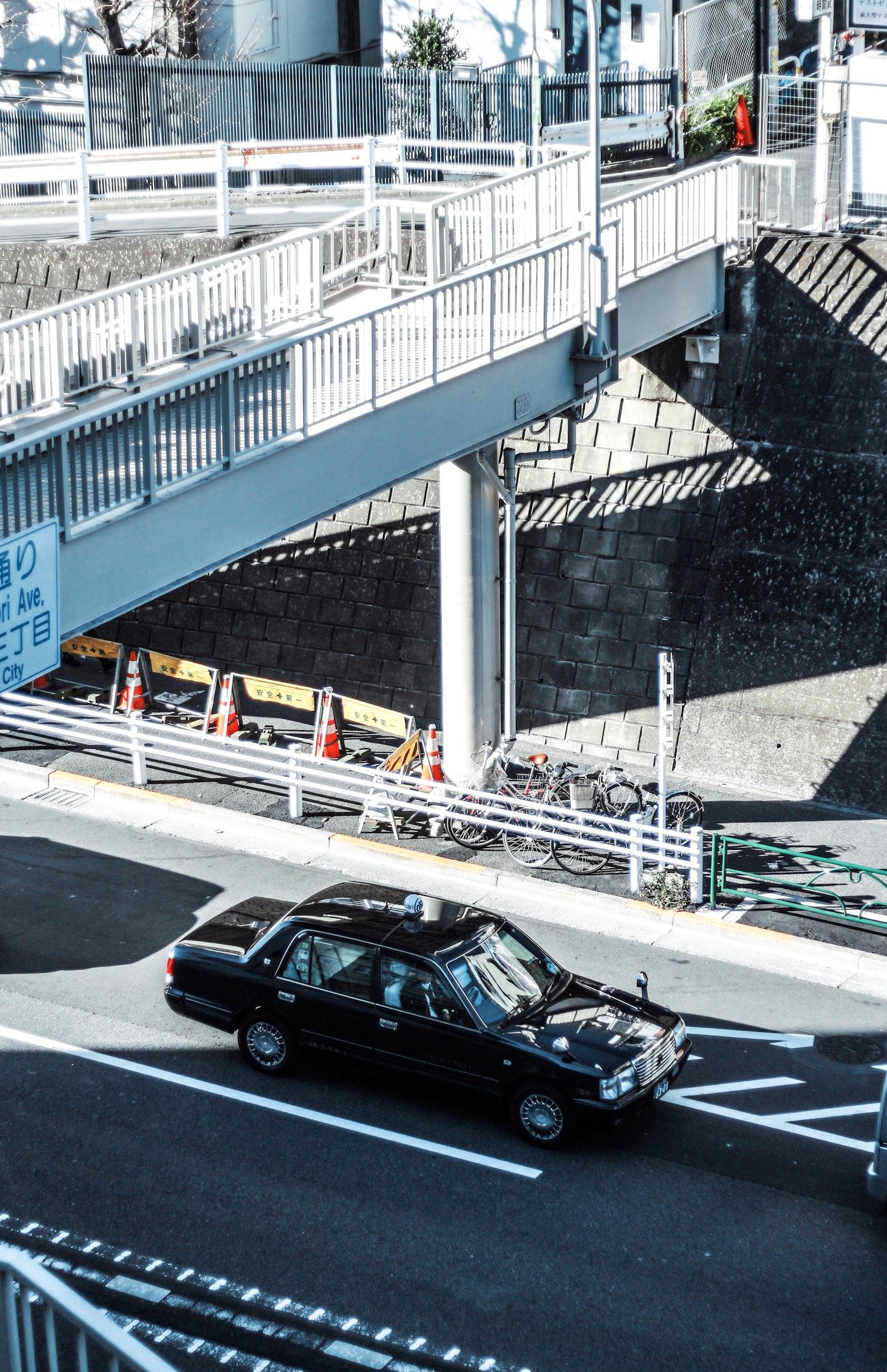 一輛黑色汽車在斑馬線附近行駛，橋下結構和陰影圖案可見