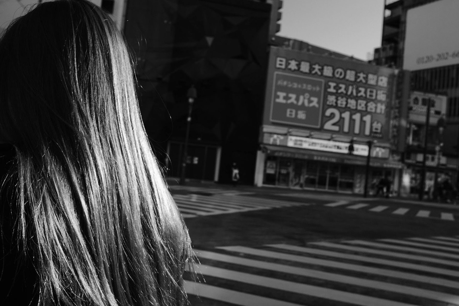 Vista posteriore di una donna con capelli lunghi in un contesto urbano con un attraversamento pedonale