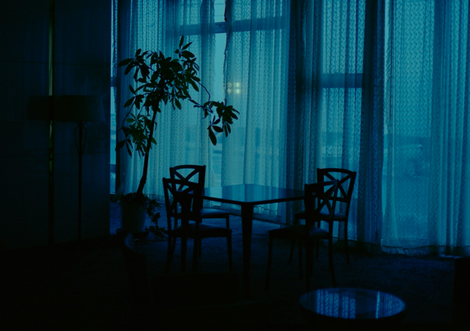 Une pièce baignée de lumière bleue avec une table et des chaises, une lumière douce filtrant à travers des rideaux transparents