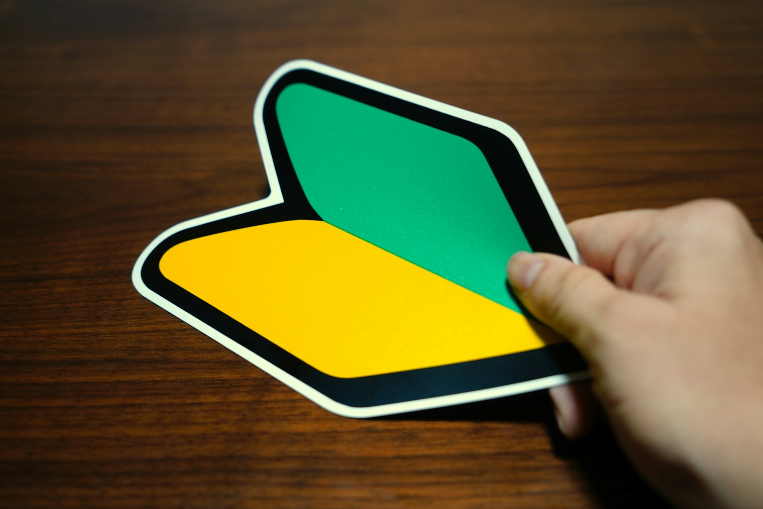 Une main tenant un autocollant simple en forme de vert et jaune