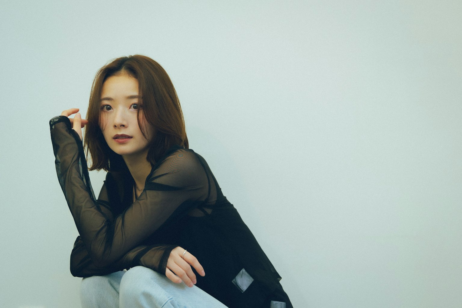 Một người phụ nữ trong áo đen và quần jean ngồi xổm dựa vào tường