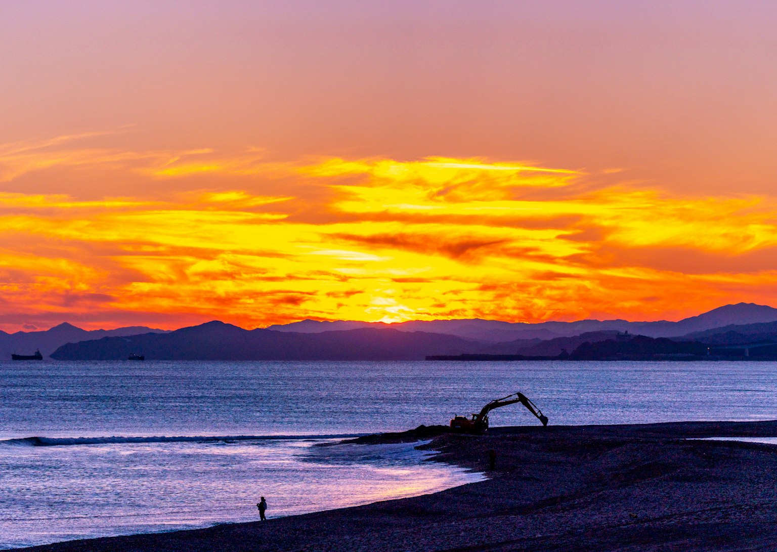 Una macchina da costruzione su una spiaggia durante un tramonto vibrante