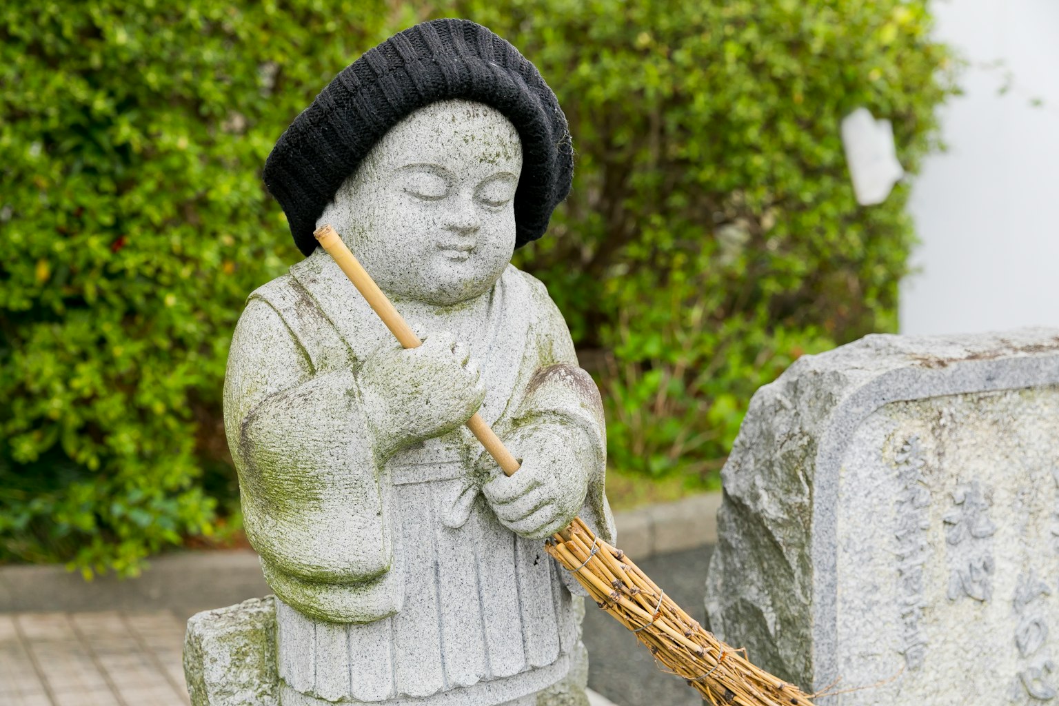 A stone statue of a child holding a broom wearing a black hat with a green background