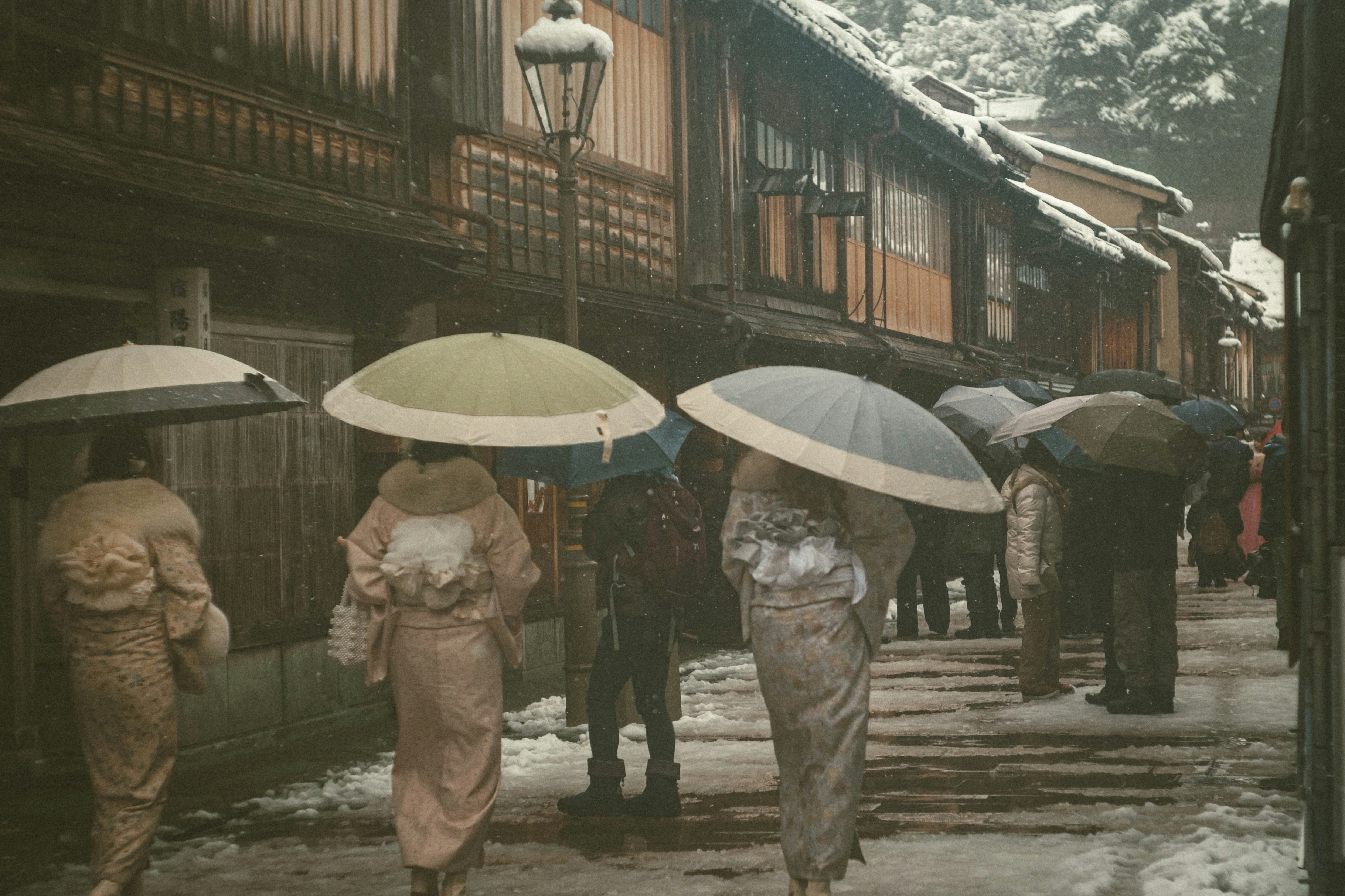 雪の路地を歩く人々と傘の並ぶレトロな町並み