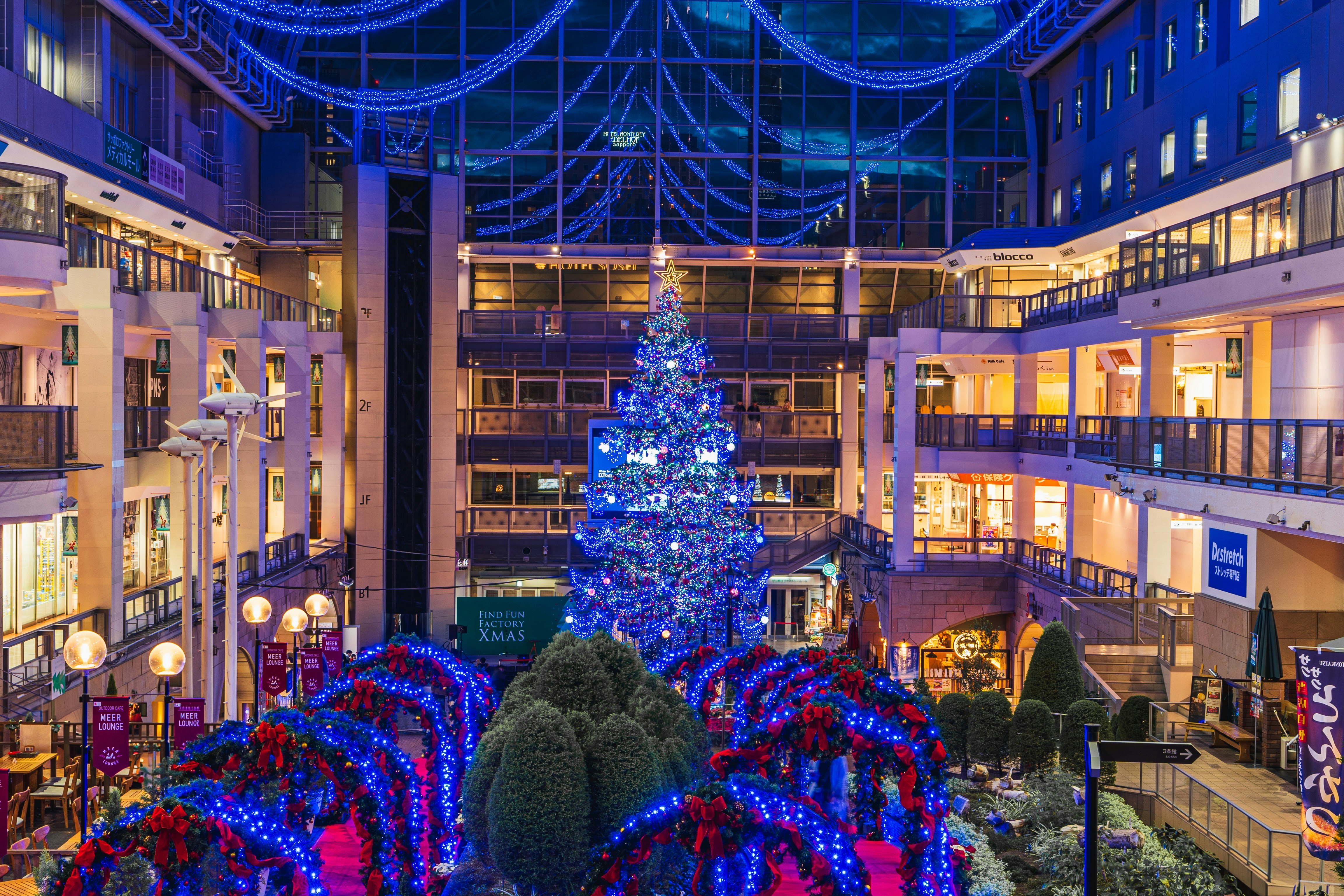 青いイルミネーションのクリスマスツリーが飾られた屋内の吹き抜け空間