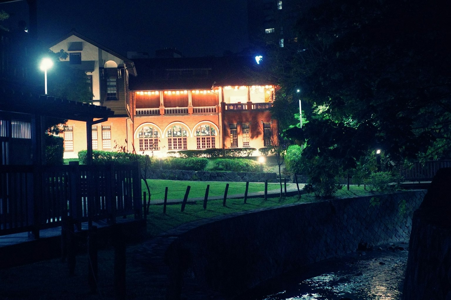 夜の川沿いにある赤レンガの建物と周囲の緑