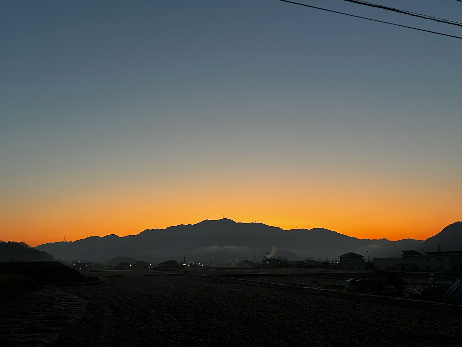 Schöne Sonnenuntergangslandschaft mit Bergsilhouetten und Feldern Helles Orange, das in tiefes Blau übergeht