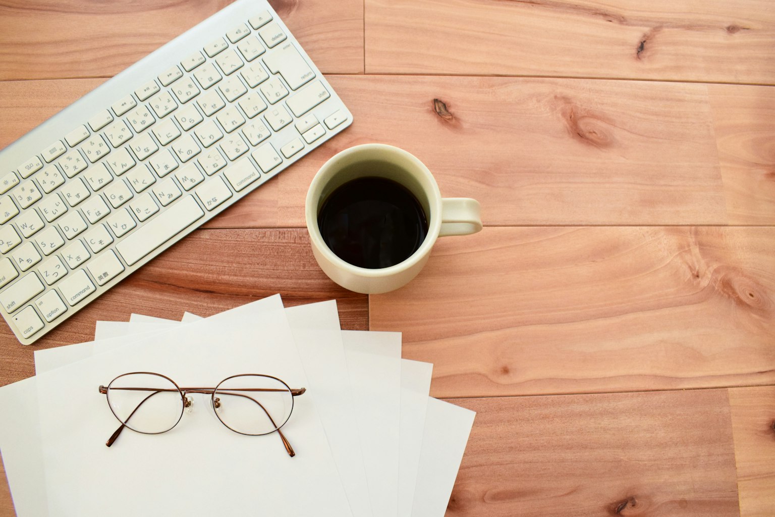 Meja kayu dengan kertas putih dan kacamata Cangkir kopi dan keyboard di dekatnya