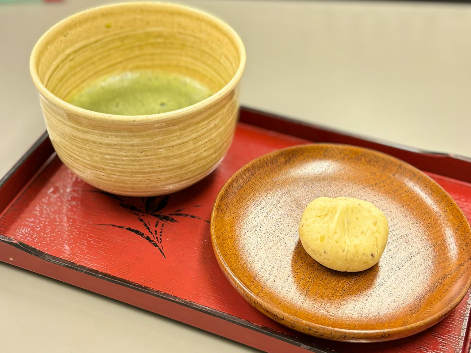 A bowl of green tea and a sweet pastry on a red tray