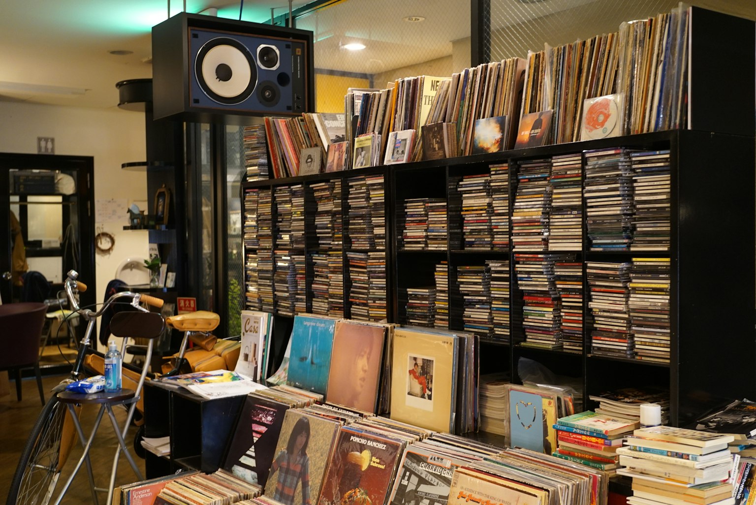 Interior de un café con estantes llenos de discos y CD junto a un altavoz