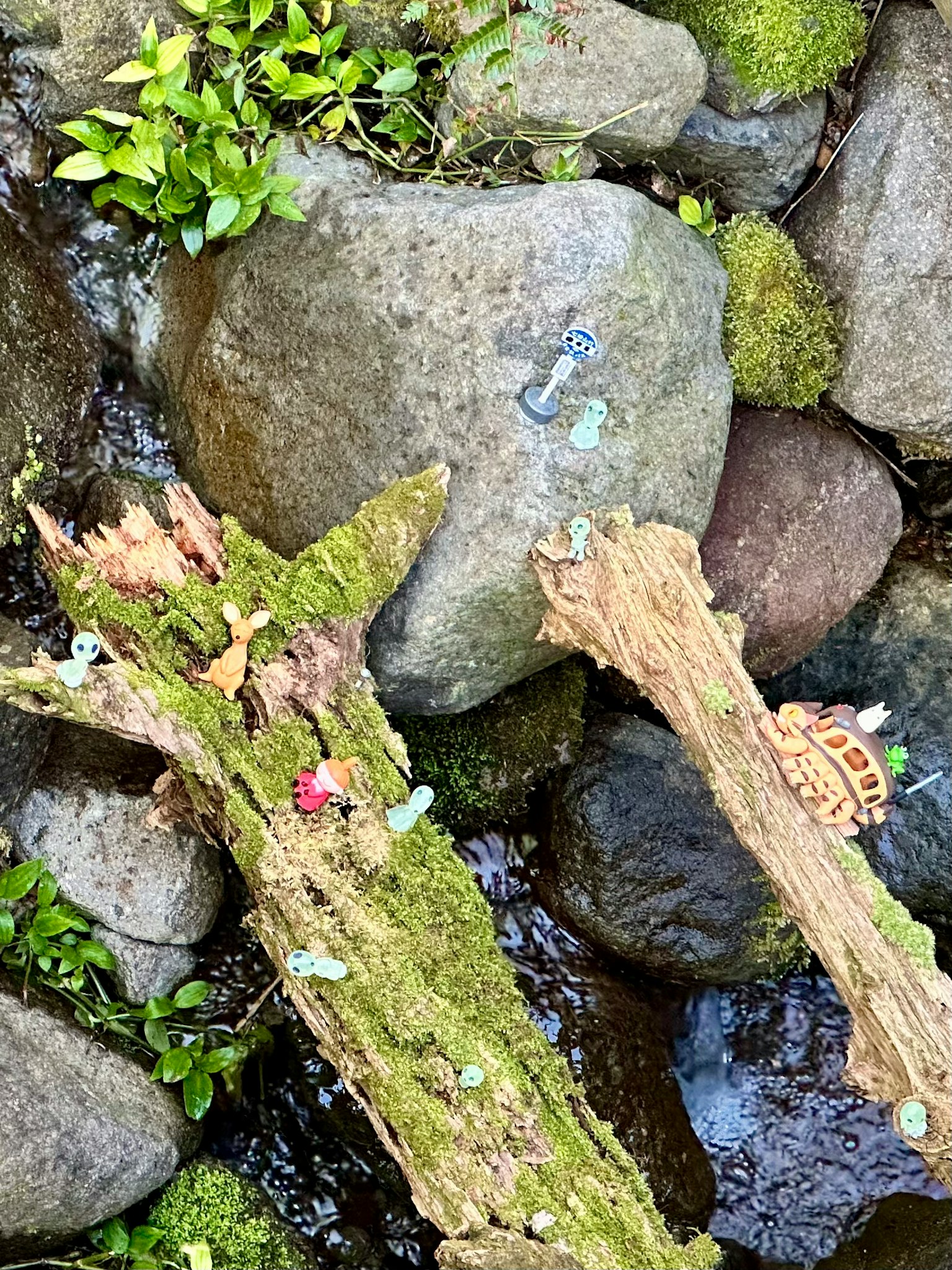 Tronchi di legno coperti di muschio e pietre in acqua corrente con piccole figurine posizionate sopra