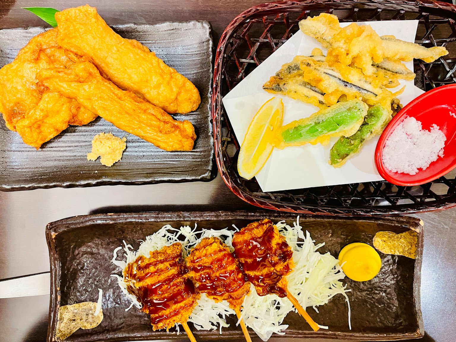 Trois plats de cuisine japonaise joliment présentés avec des fritures en haut des brochettes au centre et des tempuras avec citron en bas