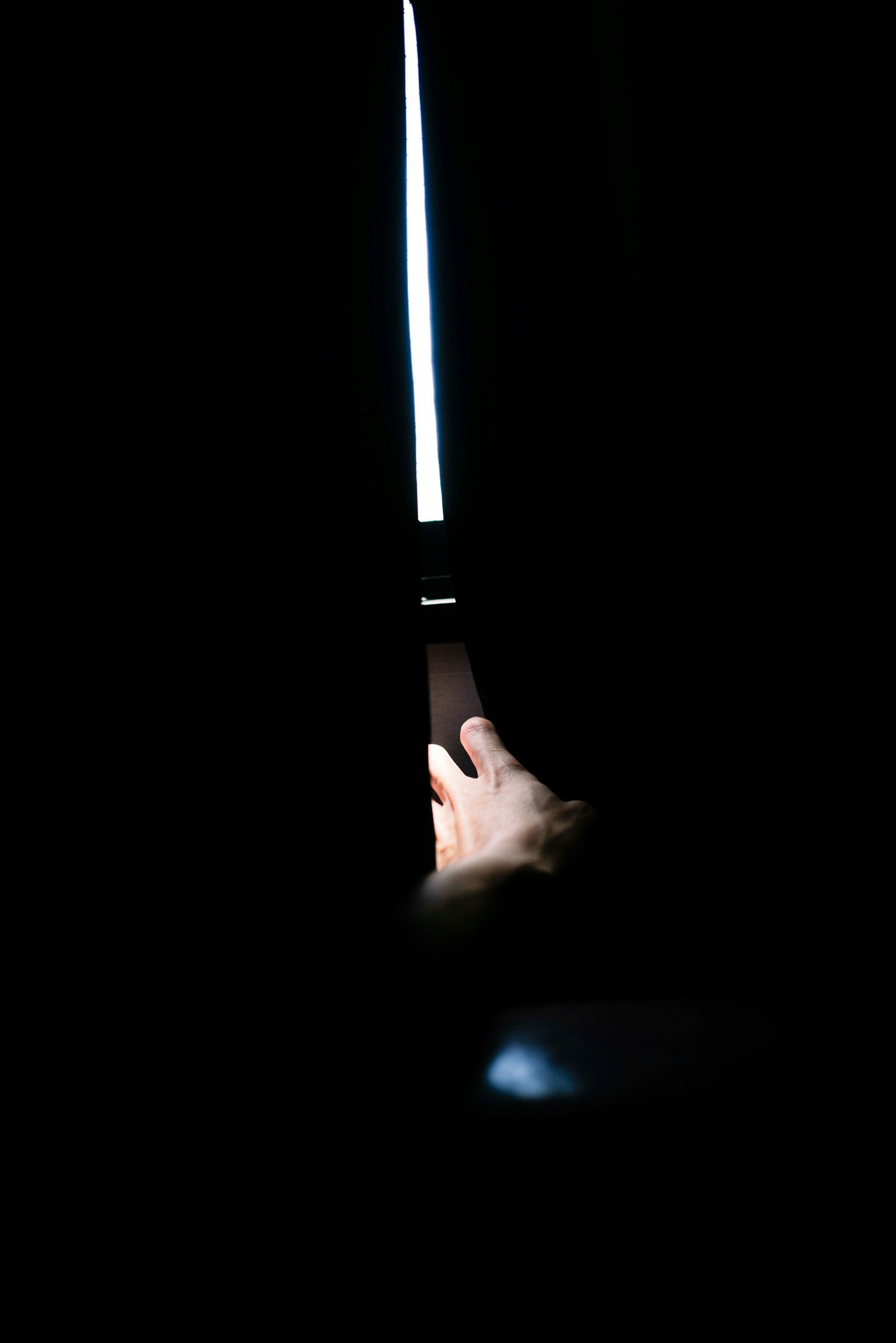 Una mano visibile attraverso una fessura in una tenda con luce che filtra dall'oscurità