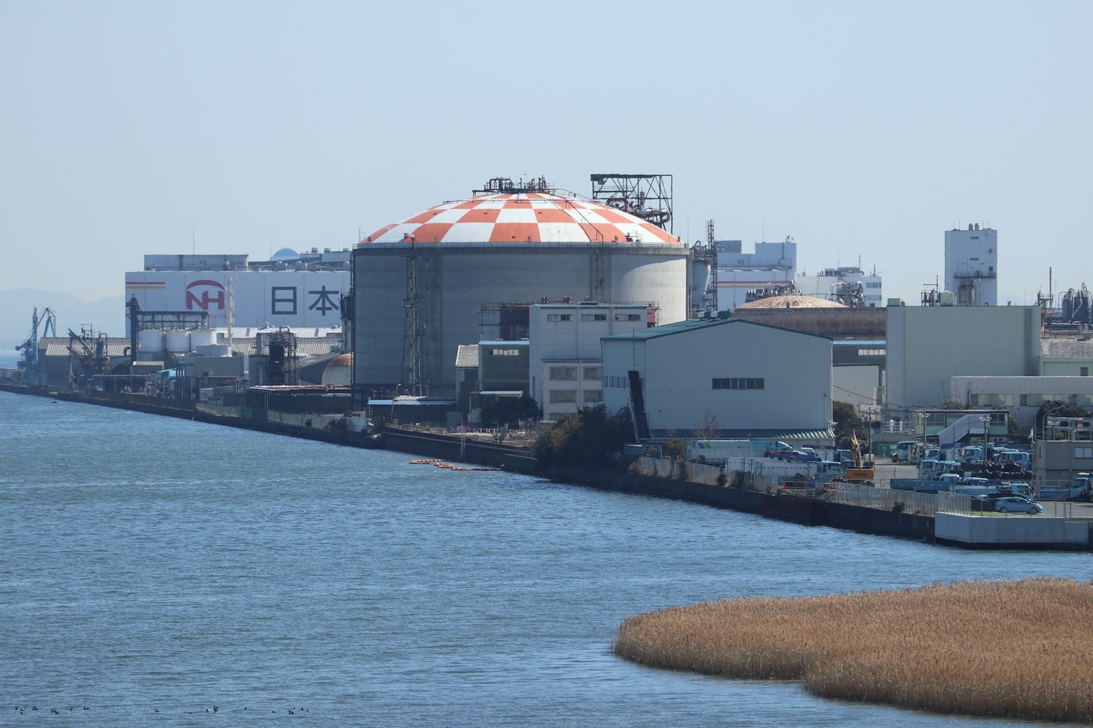 Una vista di un'area industriale lungo il fiume con un impianto dal tetto rosso e bianco e edifici vicini