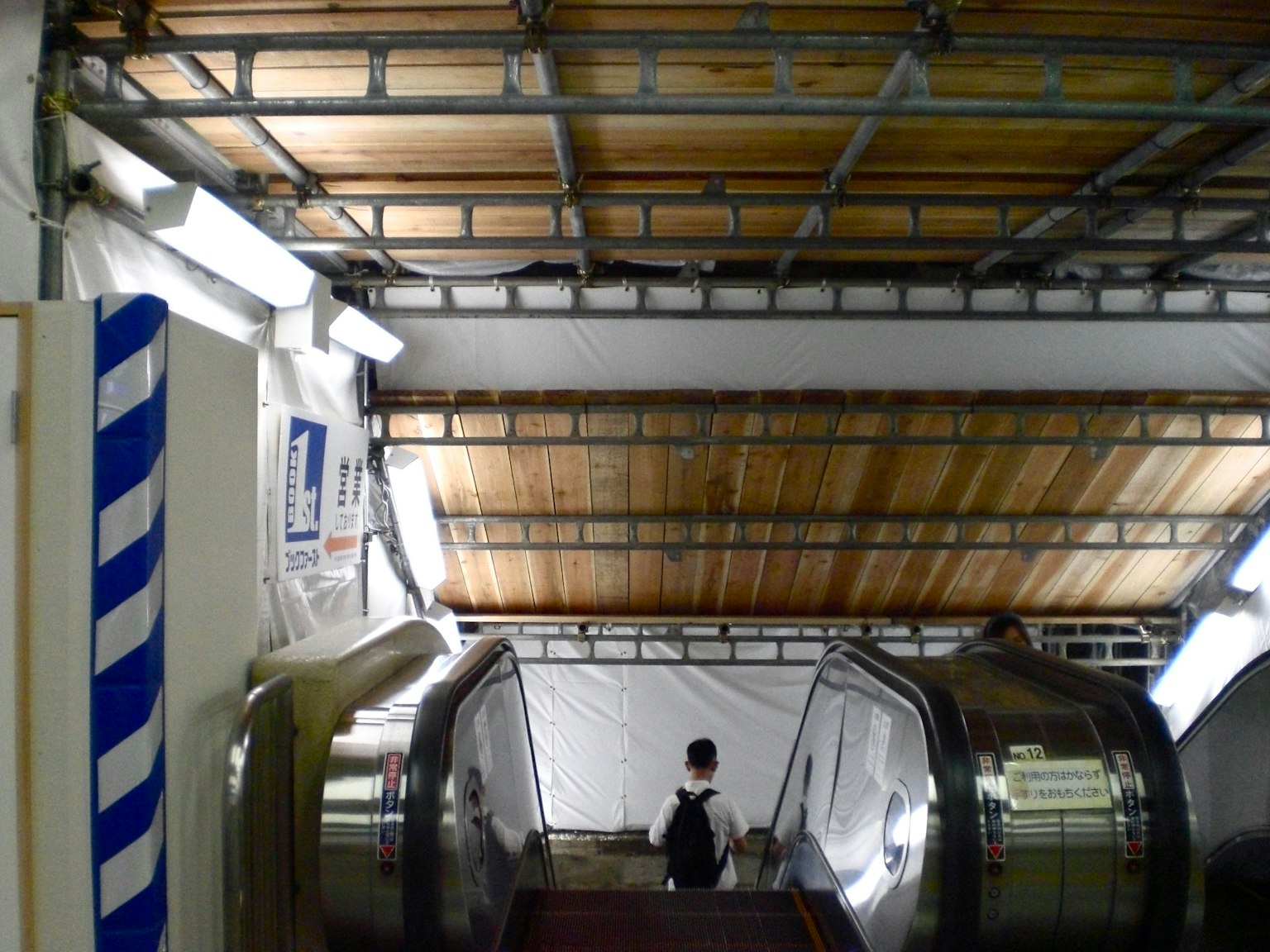 View from the bottom of an escalator featuring a metal framework ceiling white walls and wooden ceiling