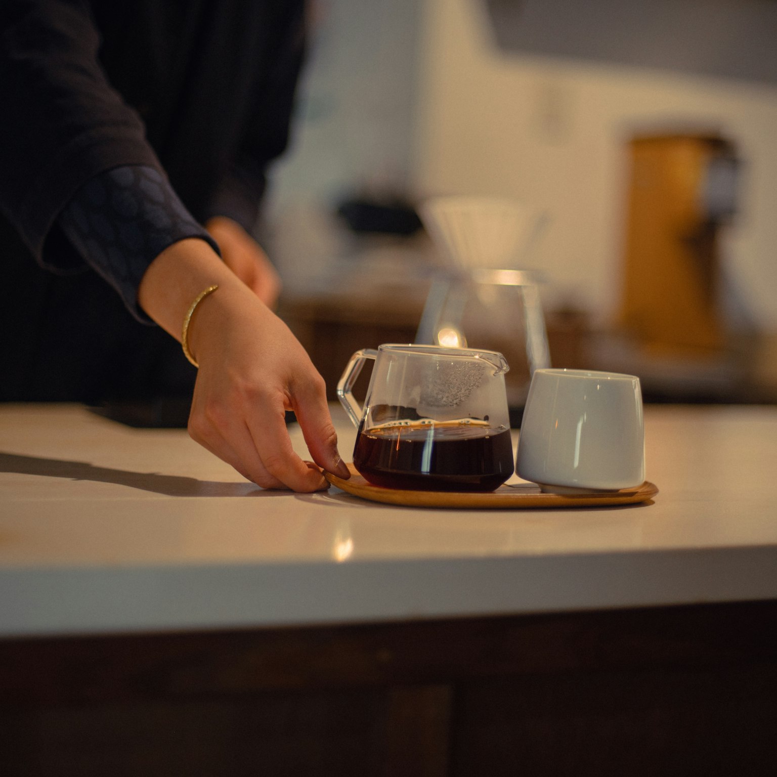 A hand pouring coffee into a white cup on a wooden tray