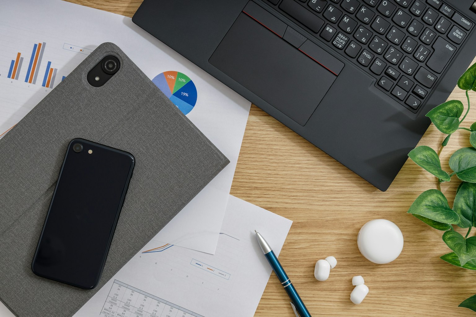 Cảnh doanh nghiệp với laptop, điện thoại thông minh, đồ thị trên giấy và cây xanh trên bàn