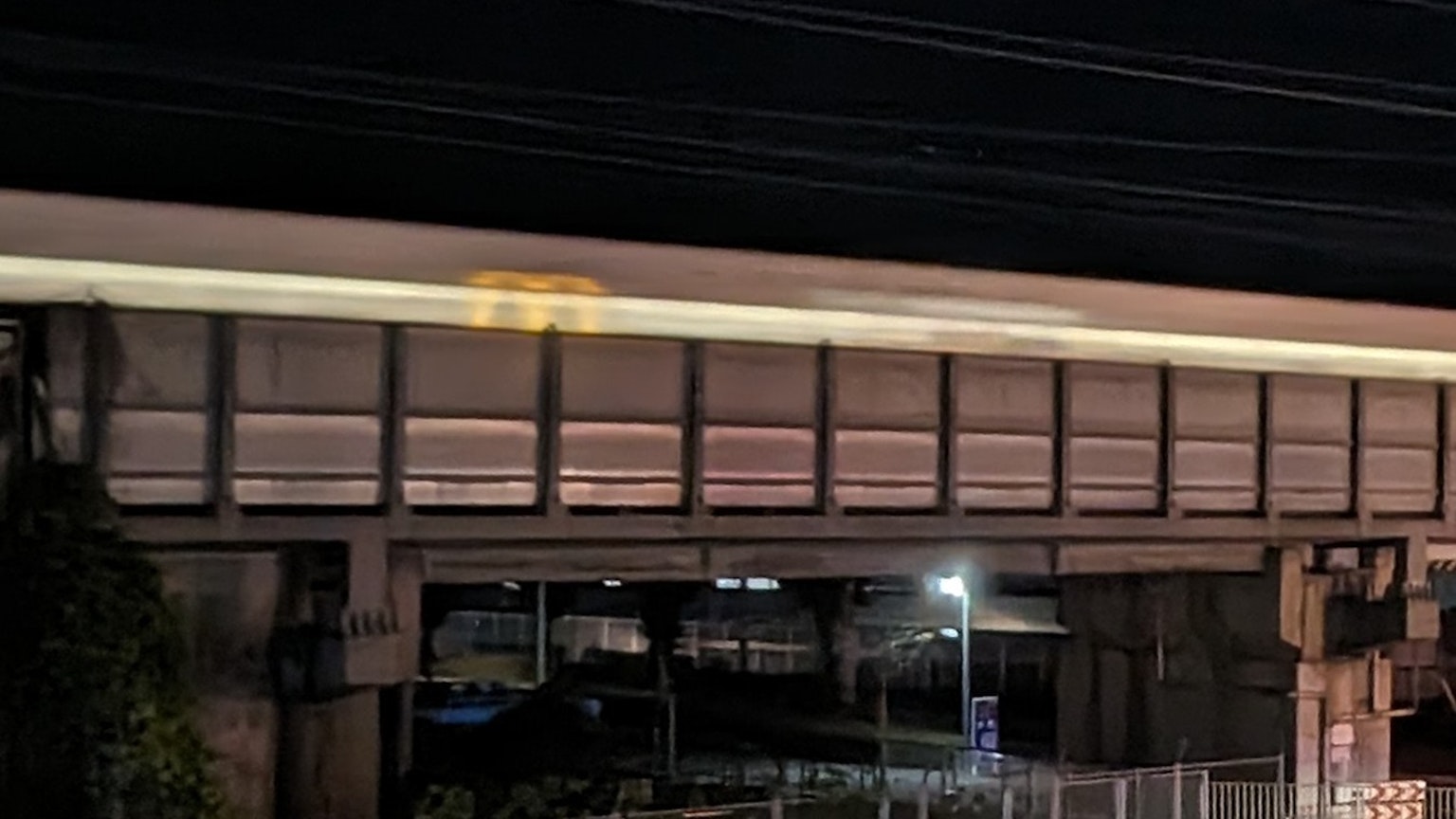 ภาพสะพานรถไฟยกระดับในเวลากลางคืนที่มีรถไฟวิ่งและไฟถนน
