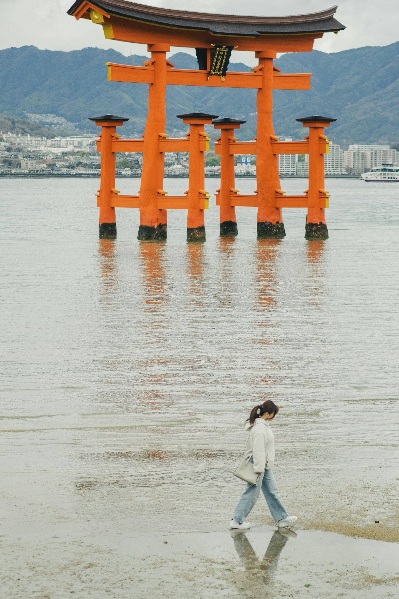 Oranger Torii-Bogen im Wasser mit einer Frau, die davor geht
