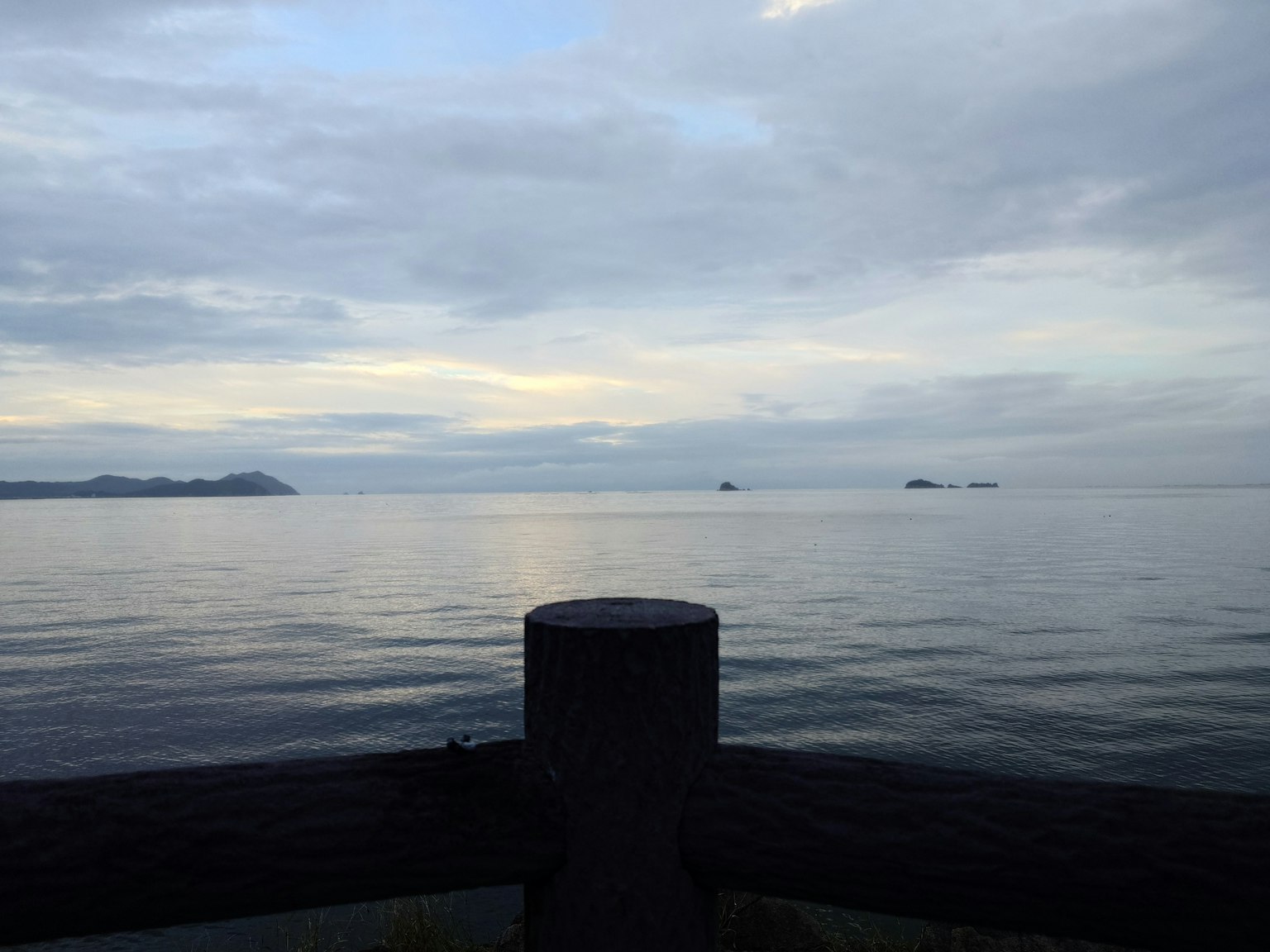 Pemandangan laut tenang dan langit berawan dengan bagian struktur di latar depan dan kapal di kejauhan