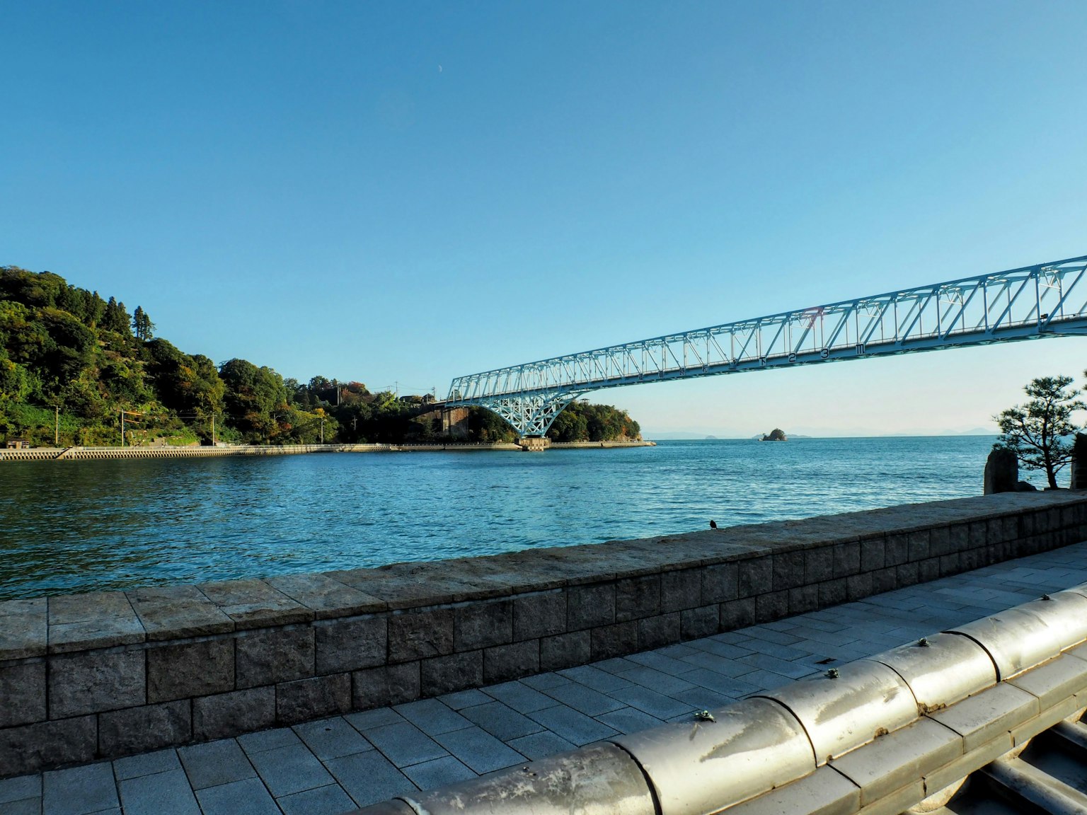 Vista panoramica di cielo blu e acqua calma con un ponte e colline verdi