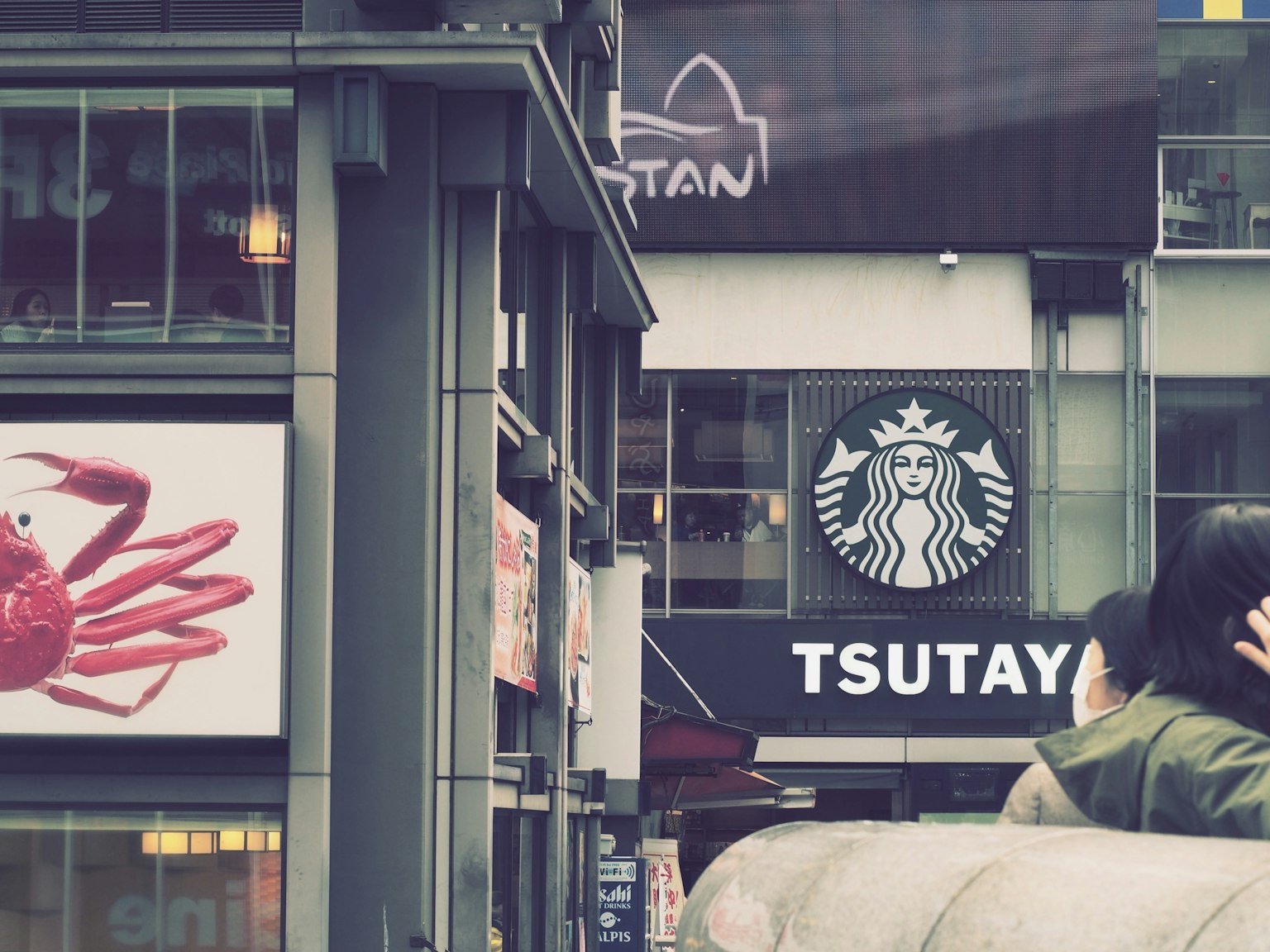 มุมถนนที่มีป้าย TSUTAYA และโลโก้ Starbucks