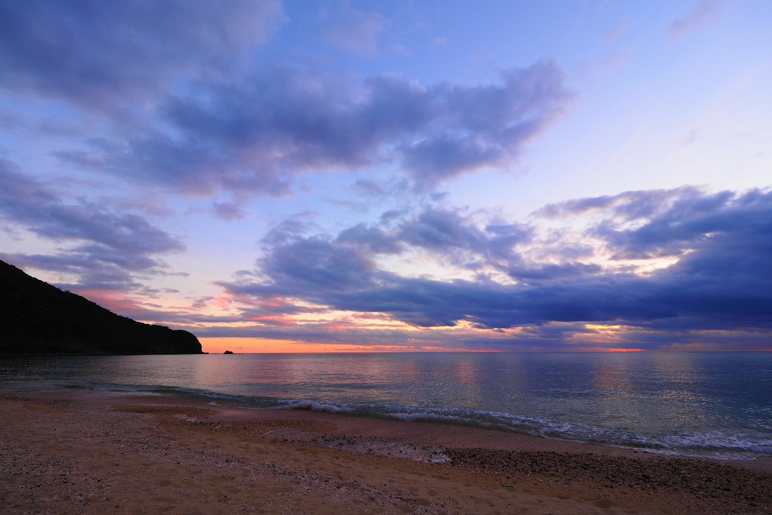ชายหาดพระอาทิตย์ตกที่สวยงามพร้อมคลื่นสงบและชายหาดทรายและท้องฟ้าสีฟ้า