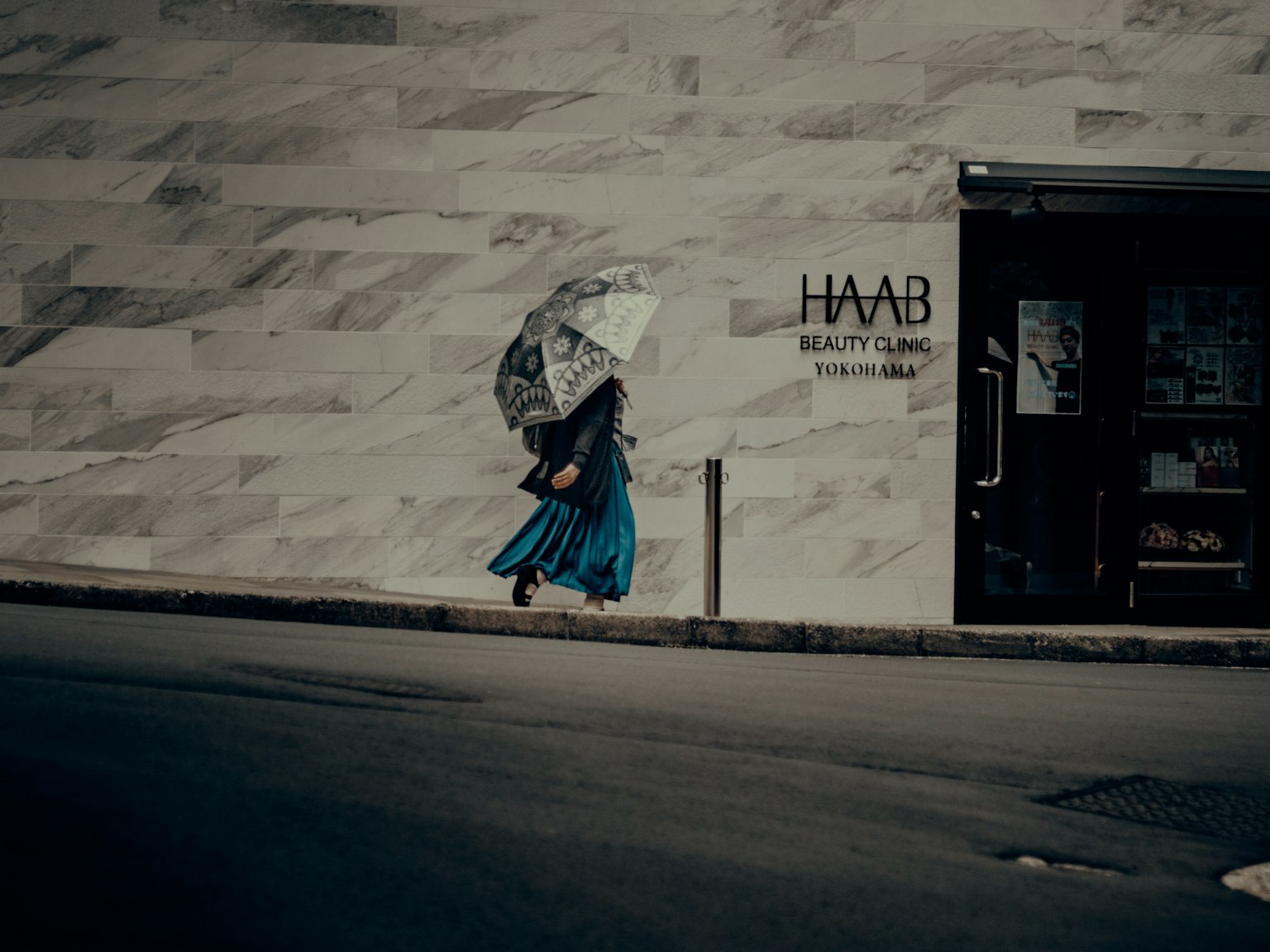 A woman in a blue skirt walking with an umbrella in an urban setting