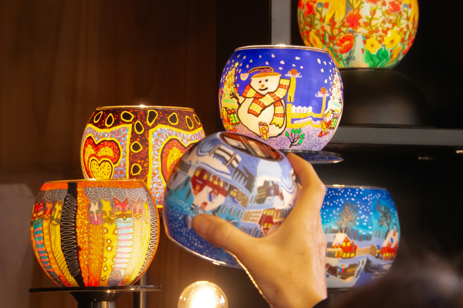 Une main levant une lampe peinte à la main colorée d'une étagère remplie de lampes variées