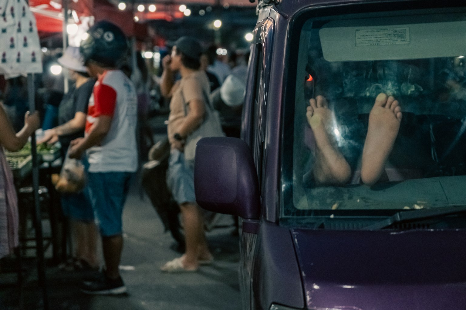 紫色の車の中に足が見える夜市の風景周囲には人々が集まっている