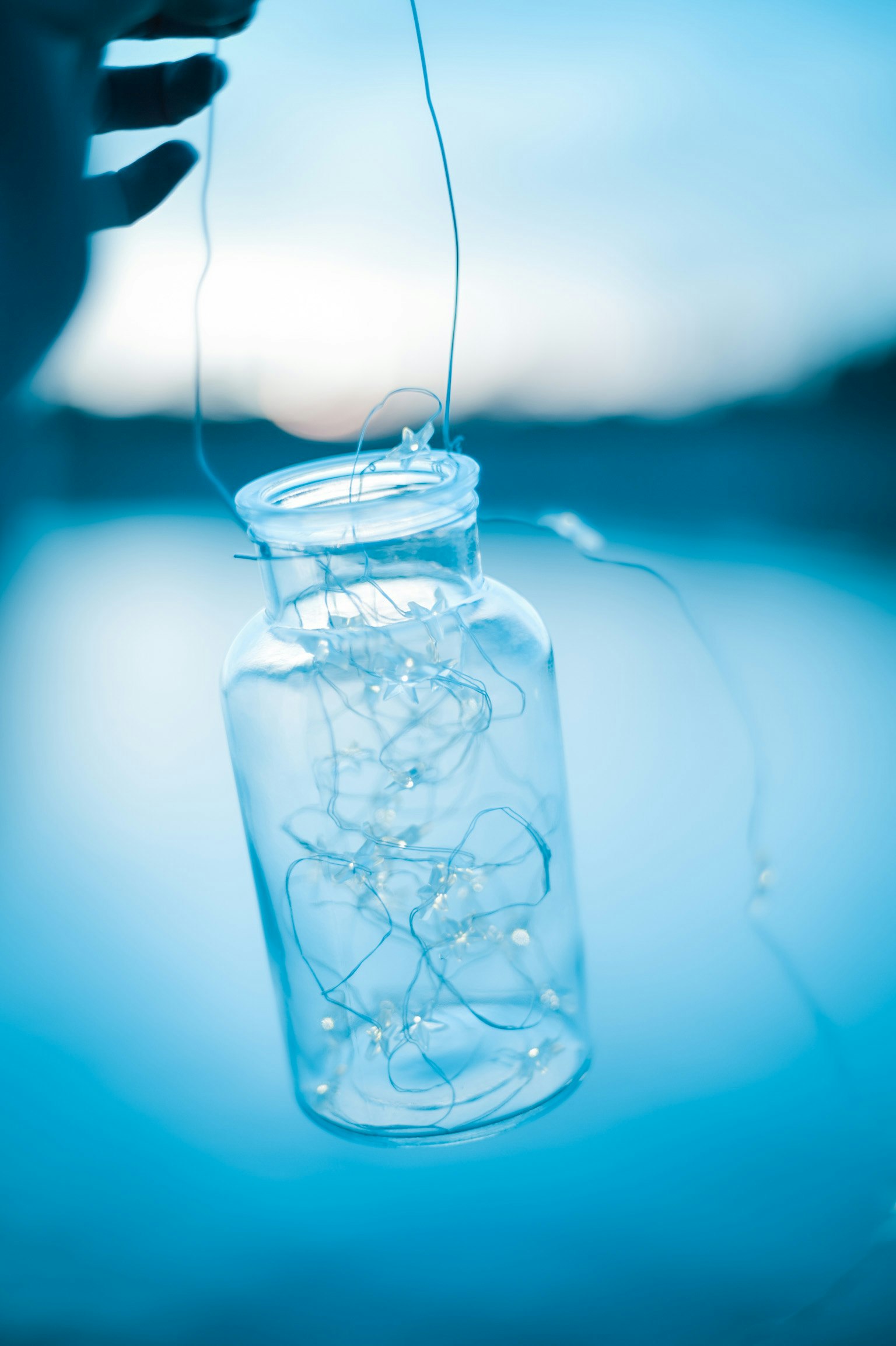 Bocal transparent tenu par une main avec des décorations lumineuses à l'intérieur sur fond bleu