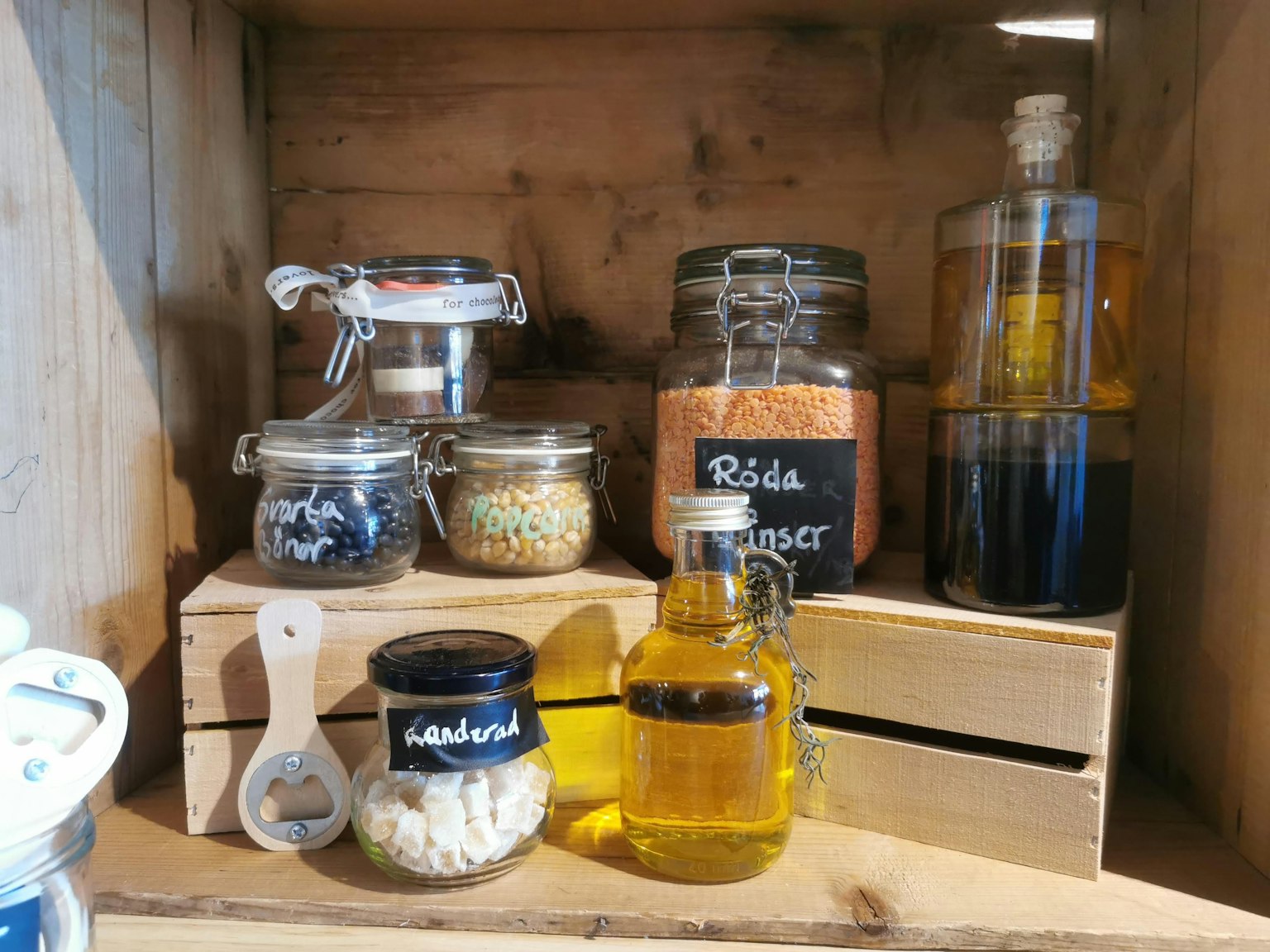 Stoples kaca dan botol minyak yang disusun di rak kayu berisi berbagai rempah dan bahan