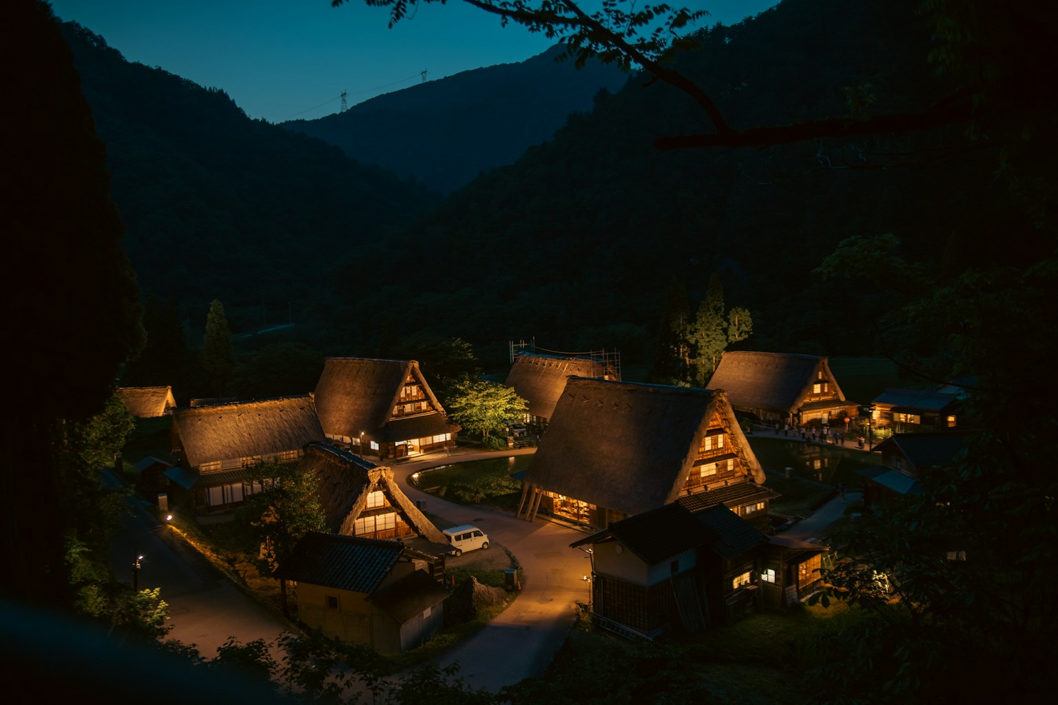 Rumah tradisional gassho-zukuri yang diterangi di malam hari di desa pegunungan