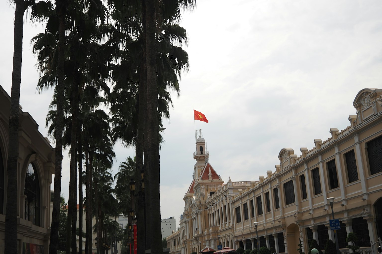 Bangunan bersejarah dengan bendera Vietnam dan pohon palem di latar depan