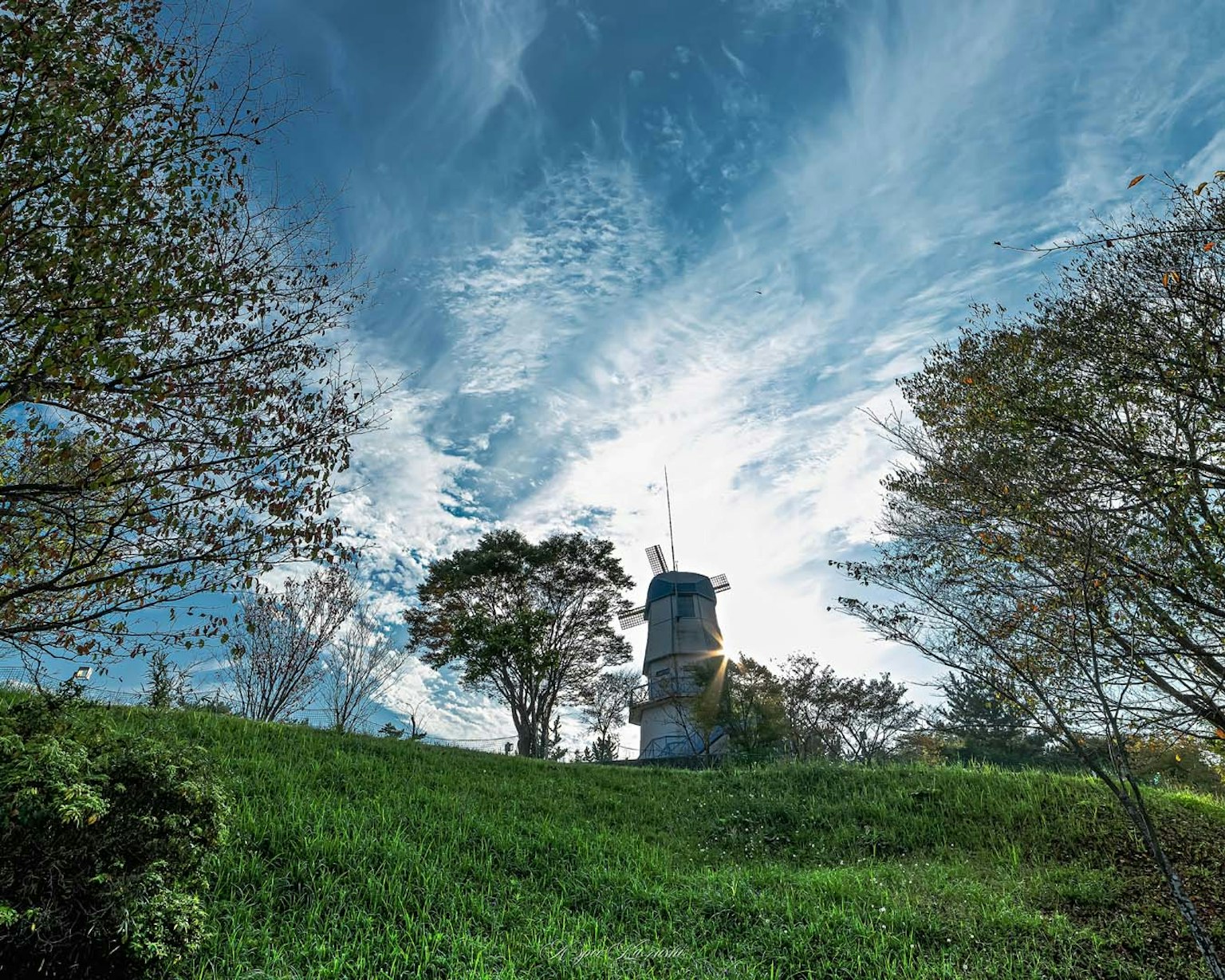 Windmill on a green hill under a blue sky with clouds