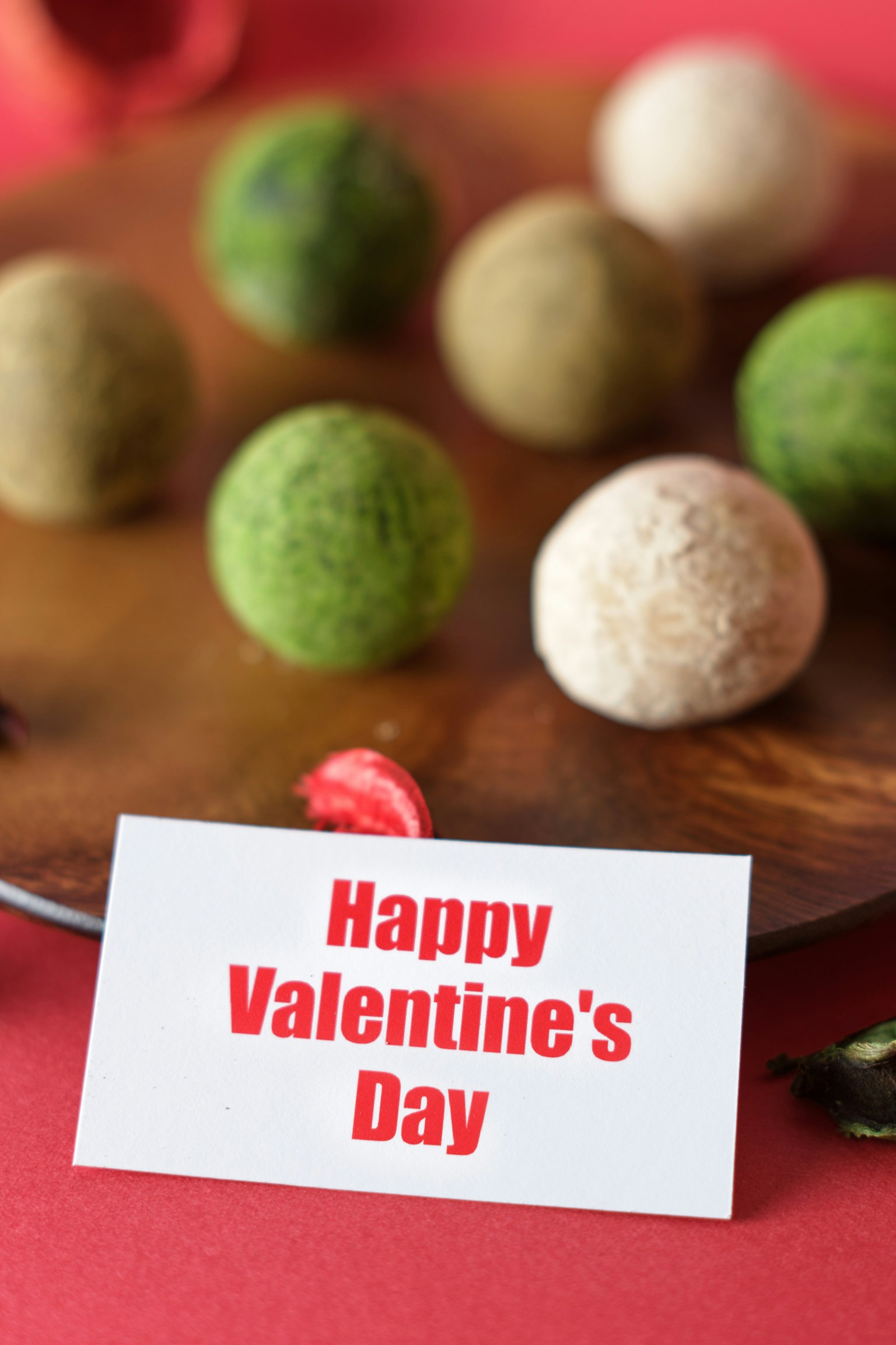 Une carte avec le message Joyeuse Saint-Valentin et des boules colorées sur une assiette en bois
