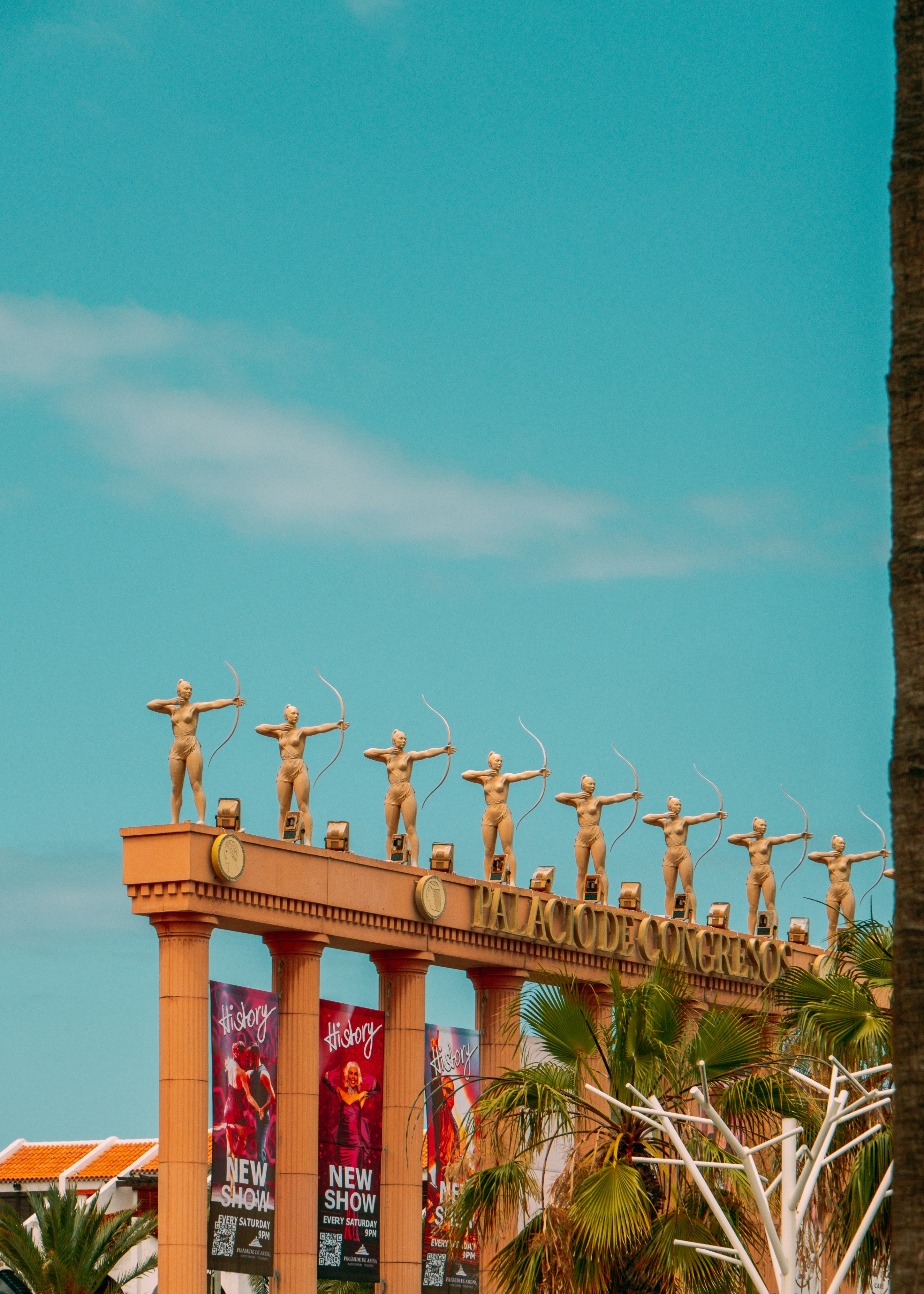 Arco exterior con una fila de estatuas humanas a lo largo de un paseo bajo un cielo azul