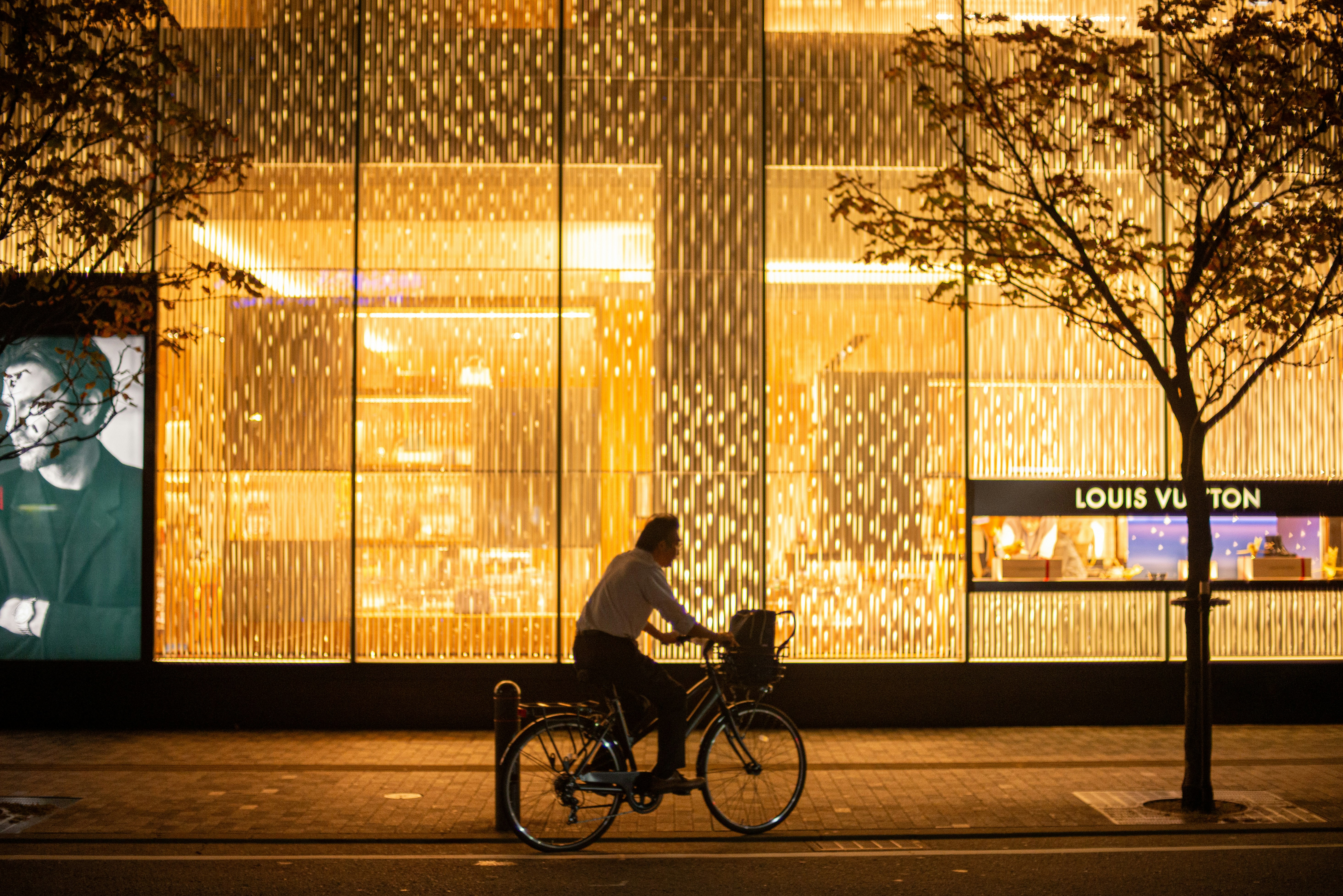 夕暮れの街角で自転車に乗る人と「LOUIS VUITTON」看板のある通り