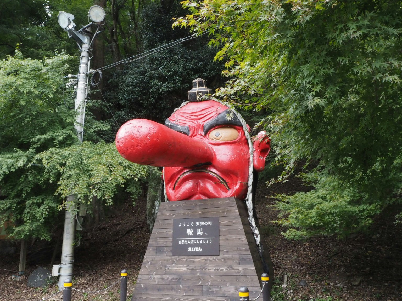 Sculpture géante avec un visage rouge et un long nez entourée d'arbres verts