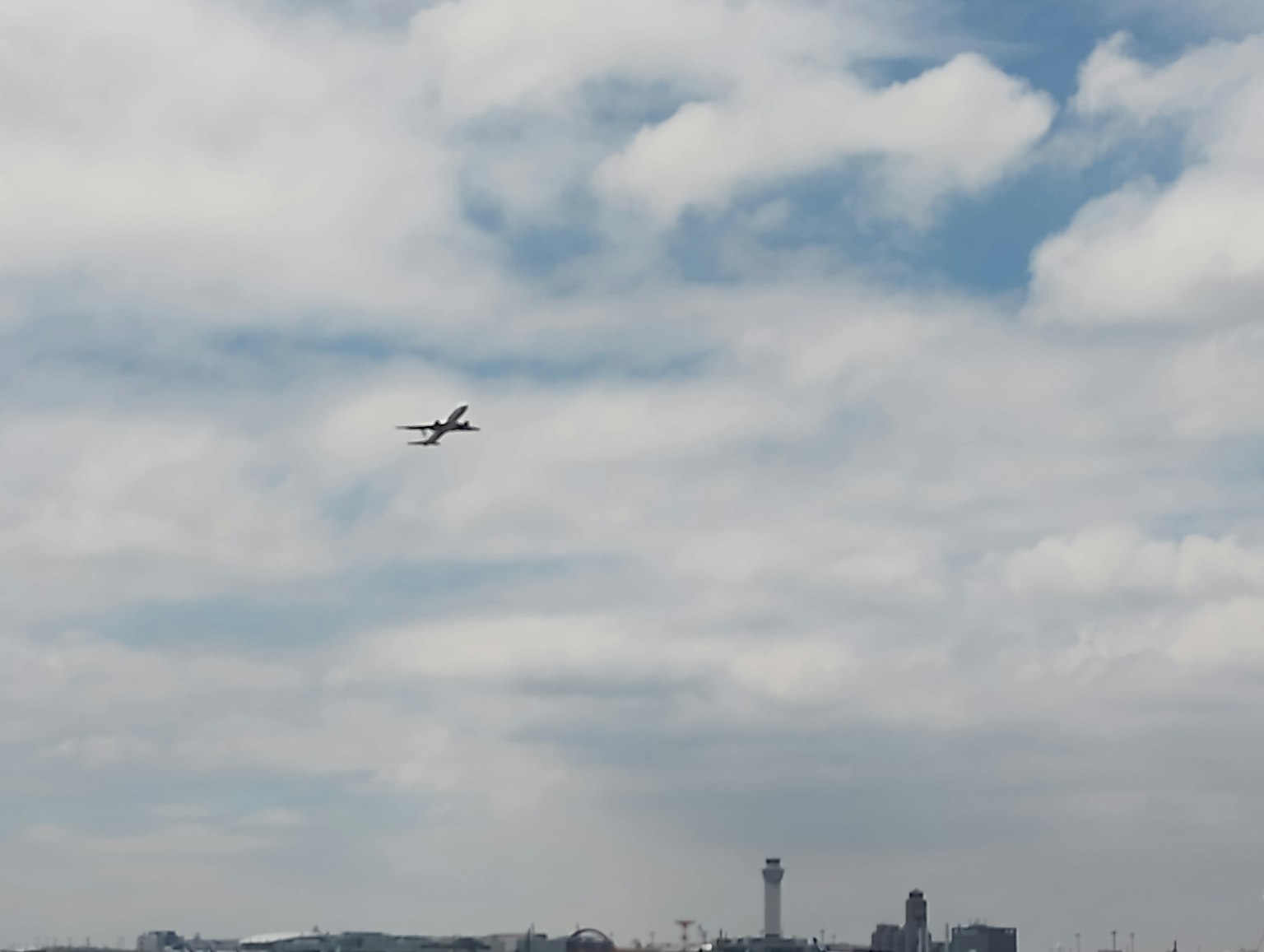 파란 하늘에서 구름 속을 나는 비행기와 멀리 보이는 공항 타워