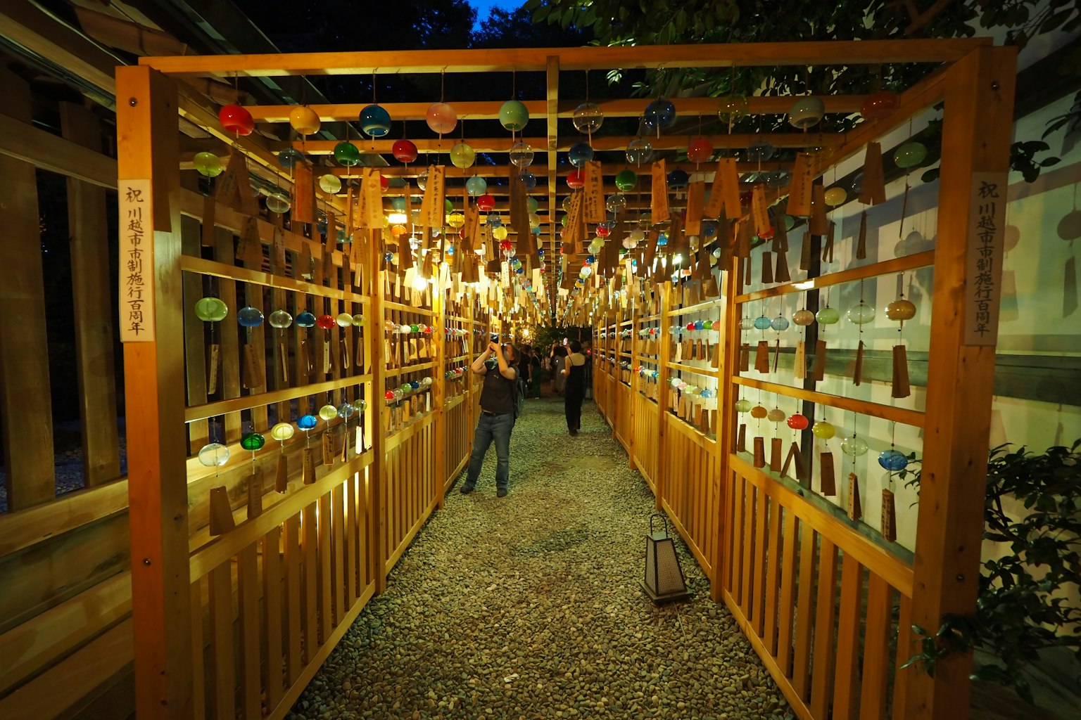 Un chemin entouré de clôtures en bois avec des décorations colorées suspendues dans la nuit