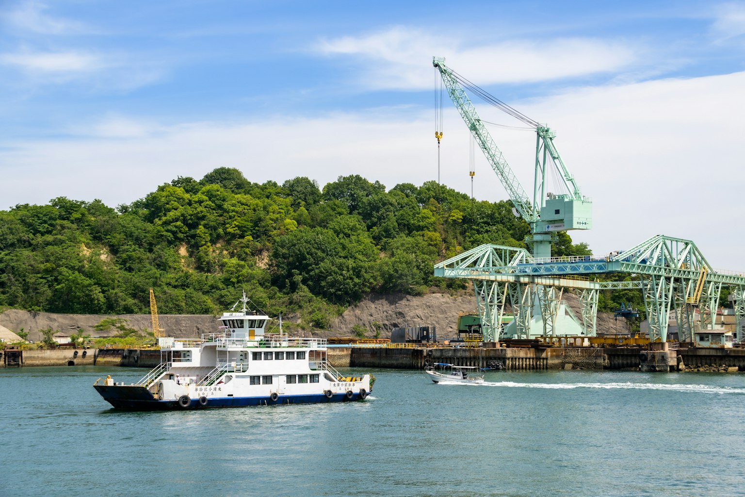 Fähre, die unter blauem Himmel in einem Hafen mit einem großen Kran im Hintergrund fährt