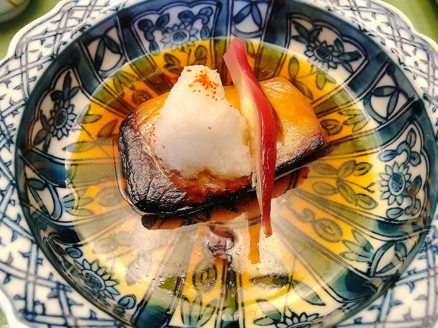 Piatto di pesce delicatamente impiattato con salsa dolce e guarnizione di daikon