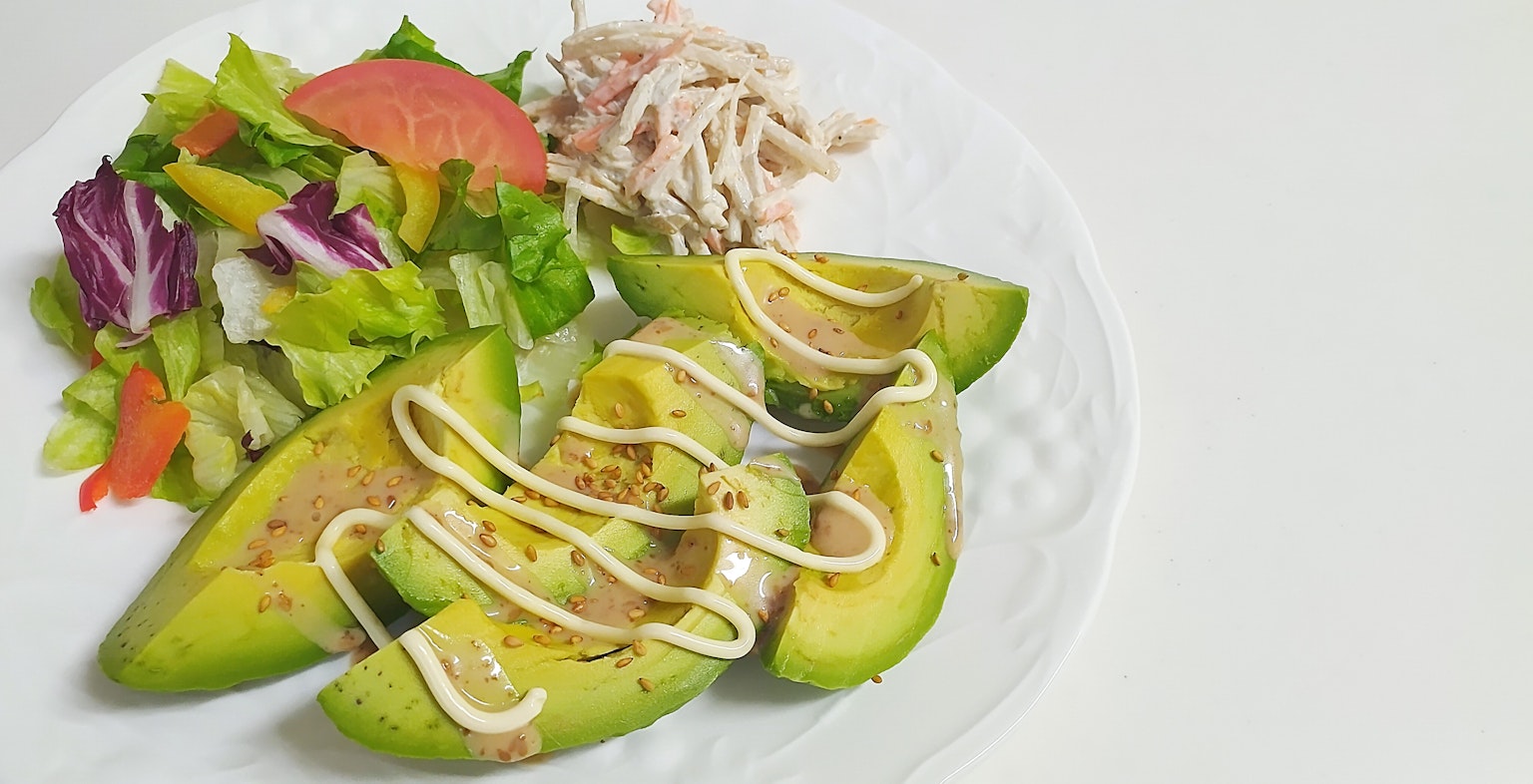 Piatto con fette di avocado con maionese e insalata a lato