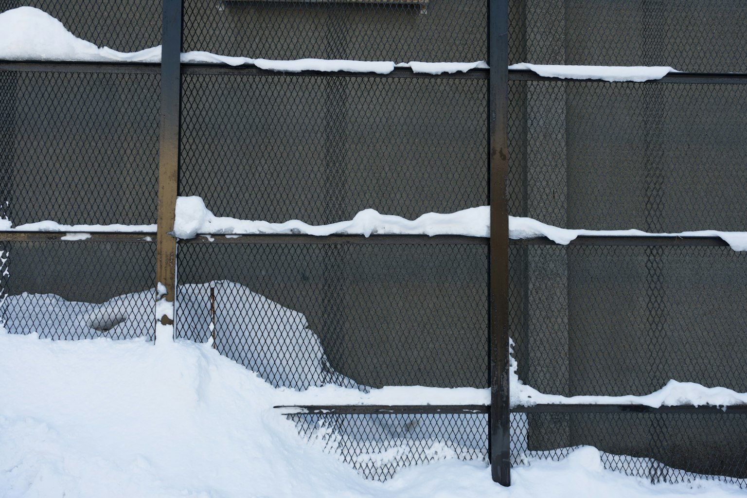 Clôture en métal recouverte de neige contre un mur en béton