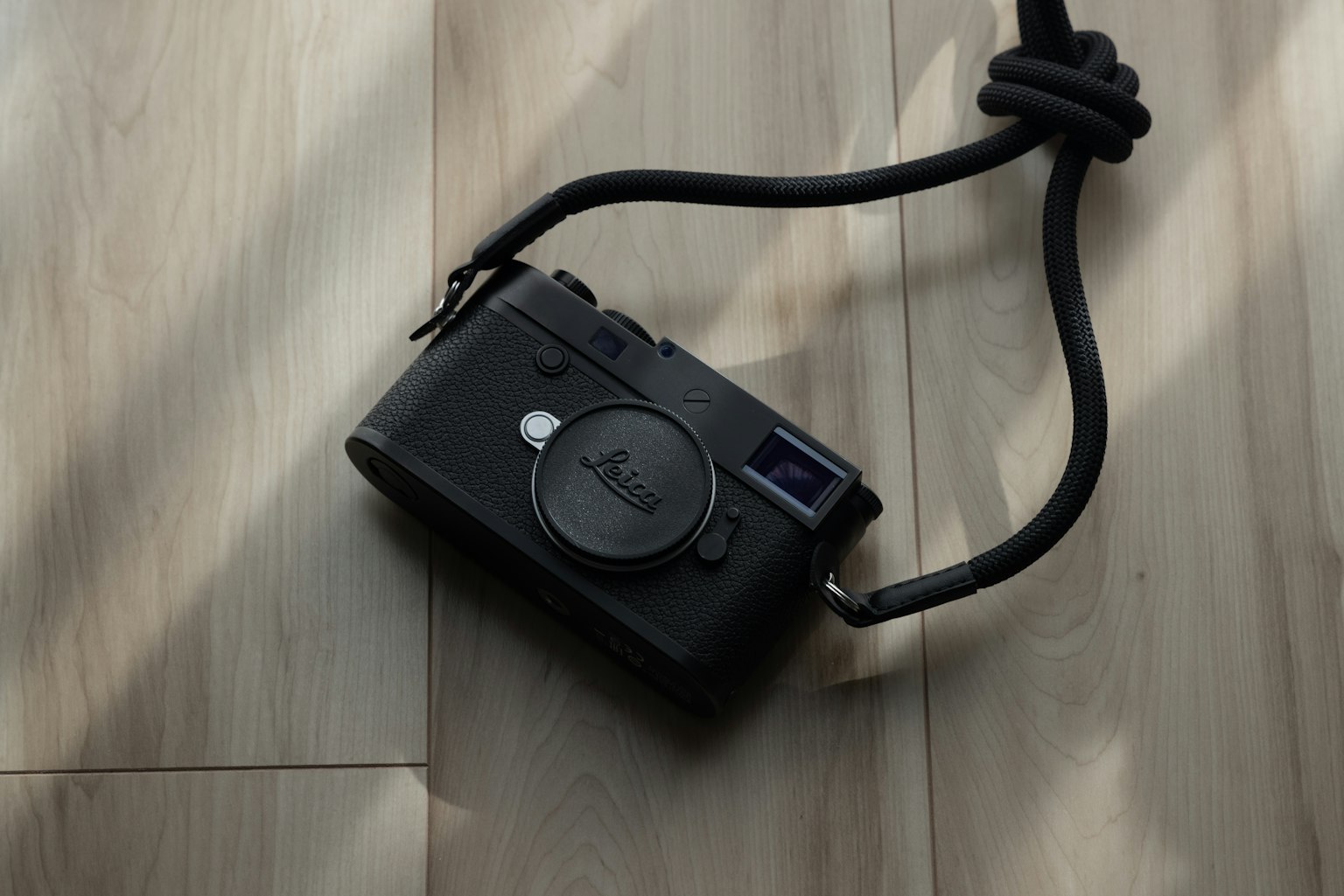 Cámara negra con una correa de cuero sobre un suelo de madera