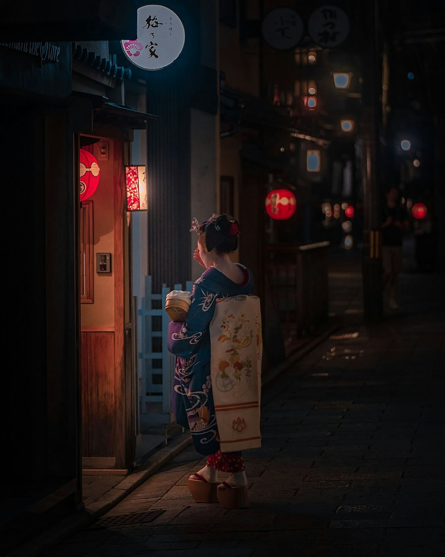 Une femme en kimono se tient devant un magasin éclairé dans une rue nocturne