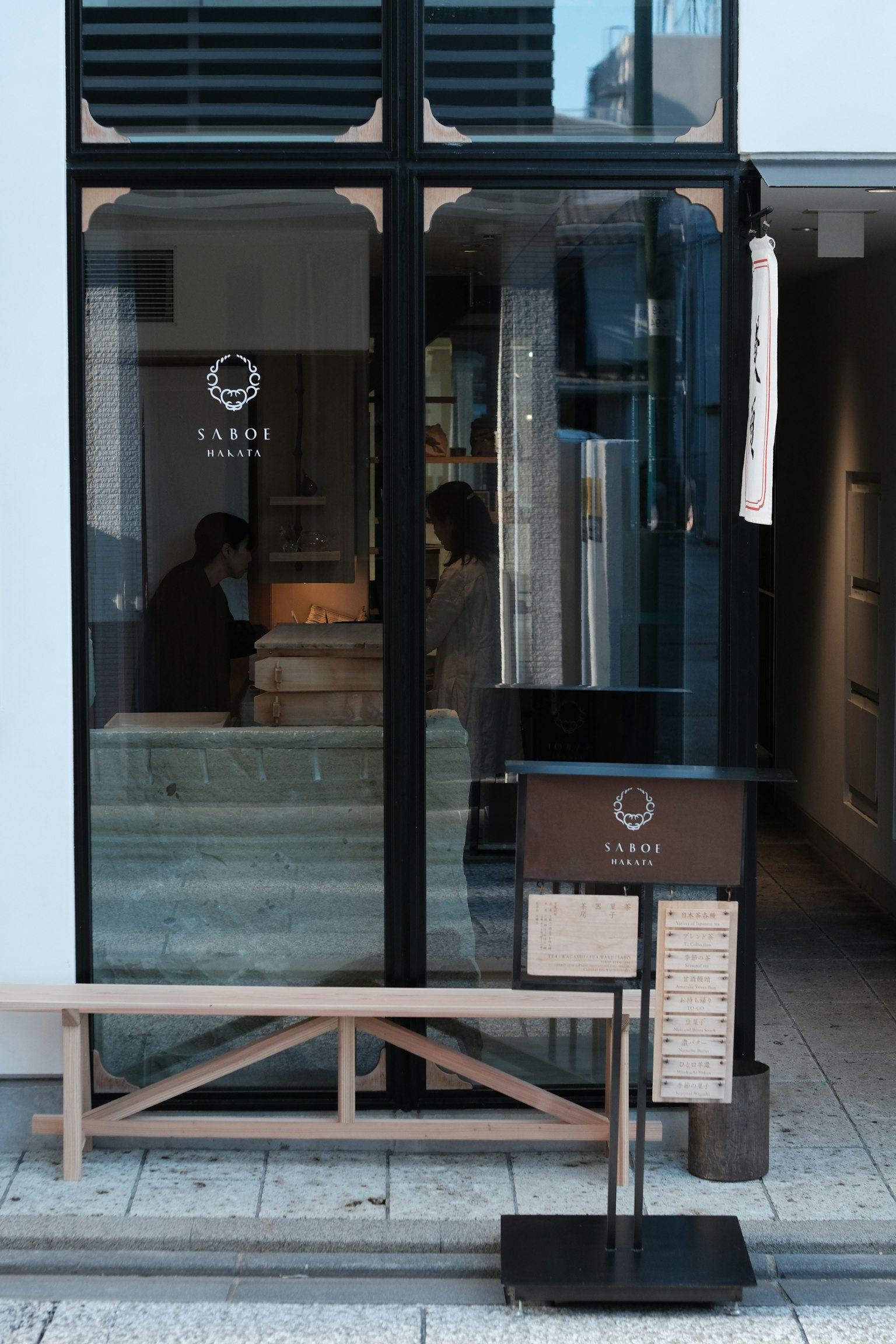 Esterno di un caffè minimalista con porte in vetro e panchina in legno