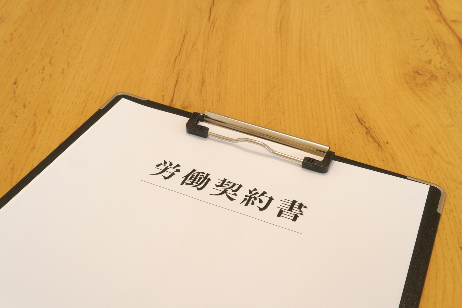 คลิปบอร์ดที่มีเอกสารสัญญาจ้างงานอยู่บนโต๊ะไม้