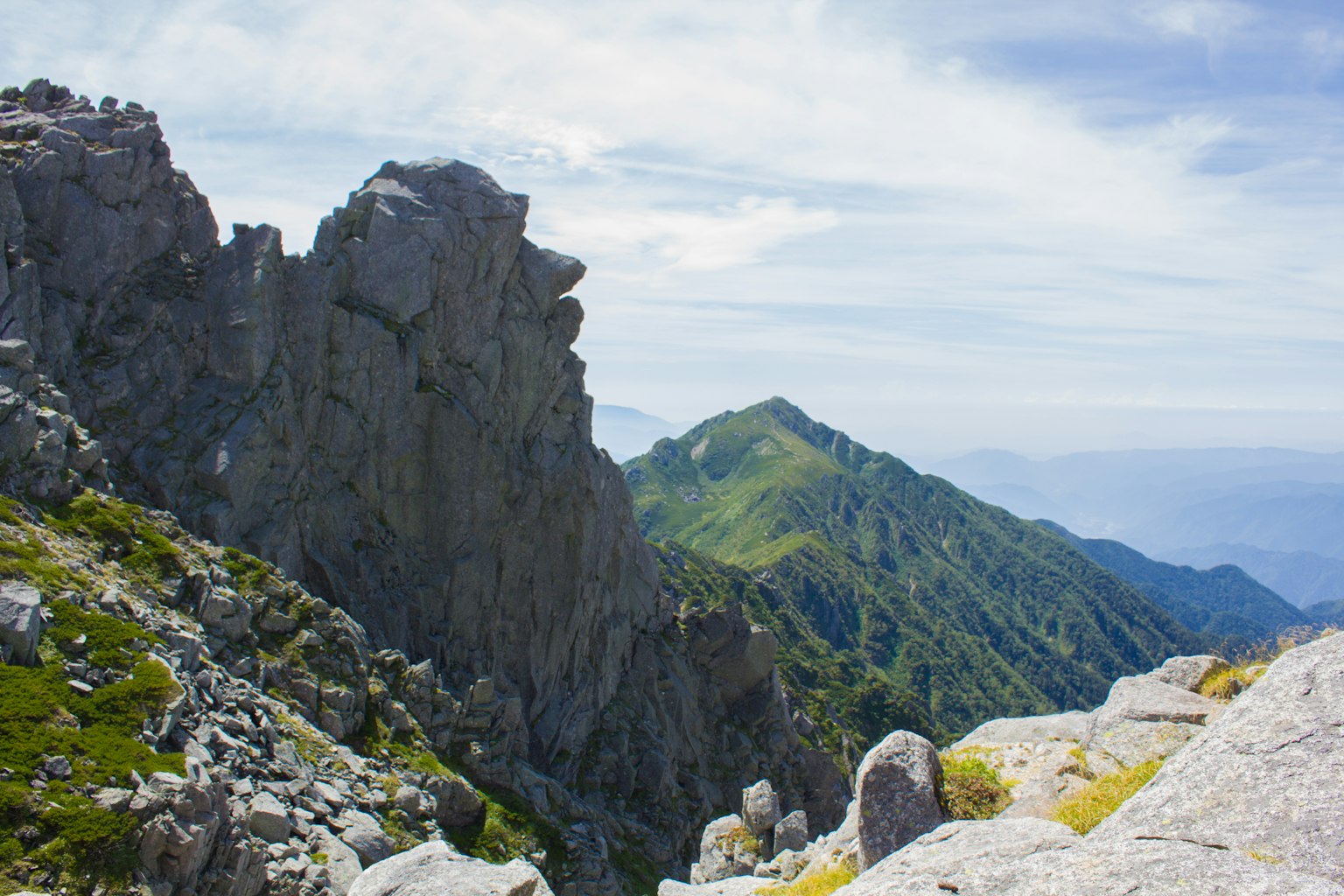 Paesaggio montano con rocce scoscese e colline verdi sotto un cielo blu